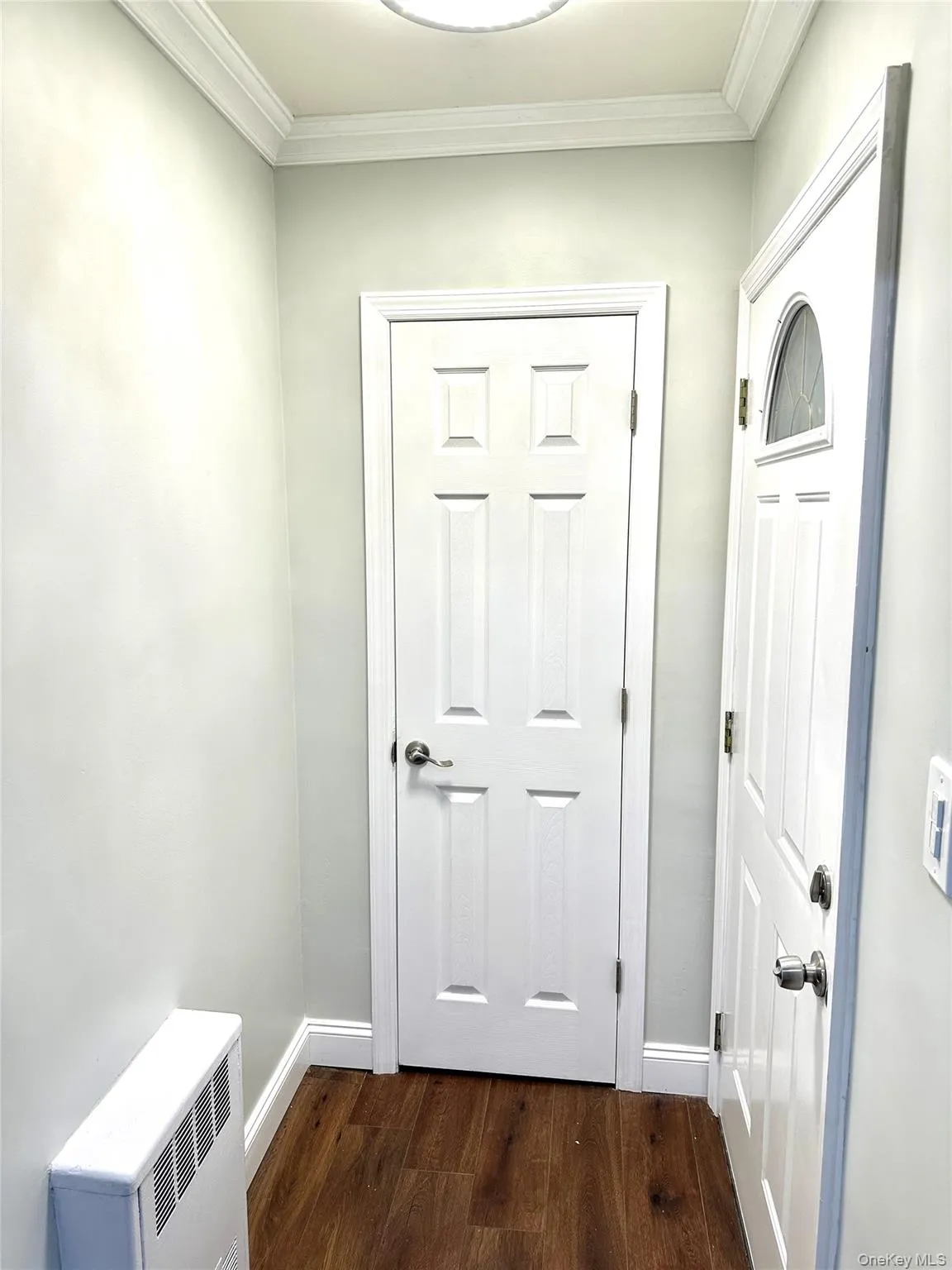 Entryway featuring wood-finish flooring, white paneled doors, crown molding, and baseboards Entryway featuring wood-finish flooring, white paneled doors, crown molding, and baseboards