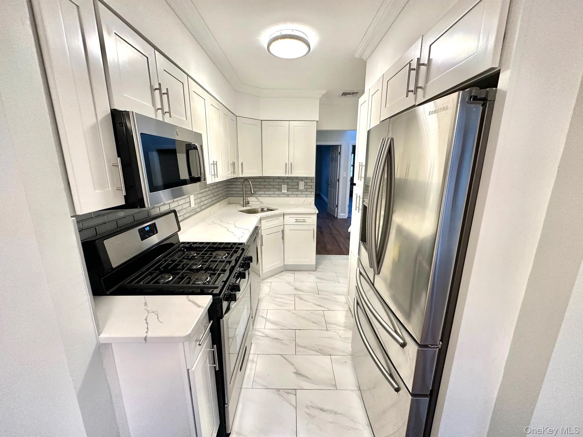 Contemporary kitchen featuring white shaker cabinetry, stainless steel appliances, white countertops, and a gray subway tile backsplash Contemporary kitchen featuring white shaker cabinetry, stainless steel appliances, white countertops, and a gray subway tile backsplash