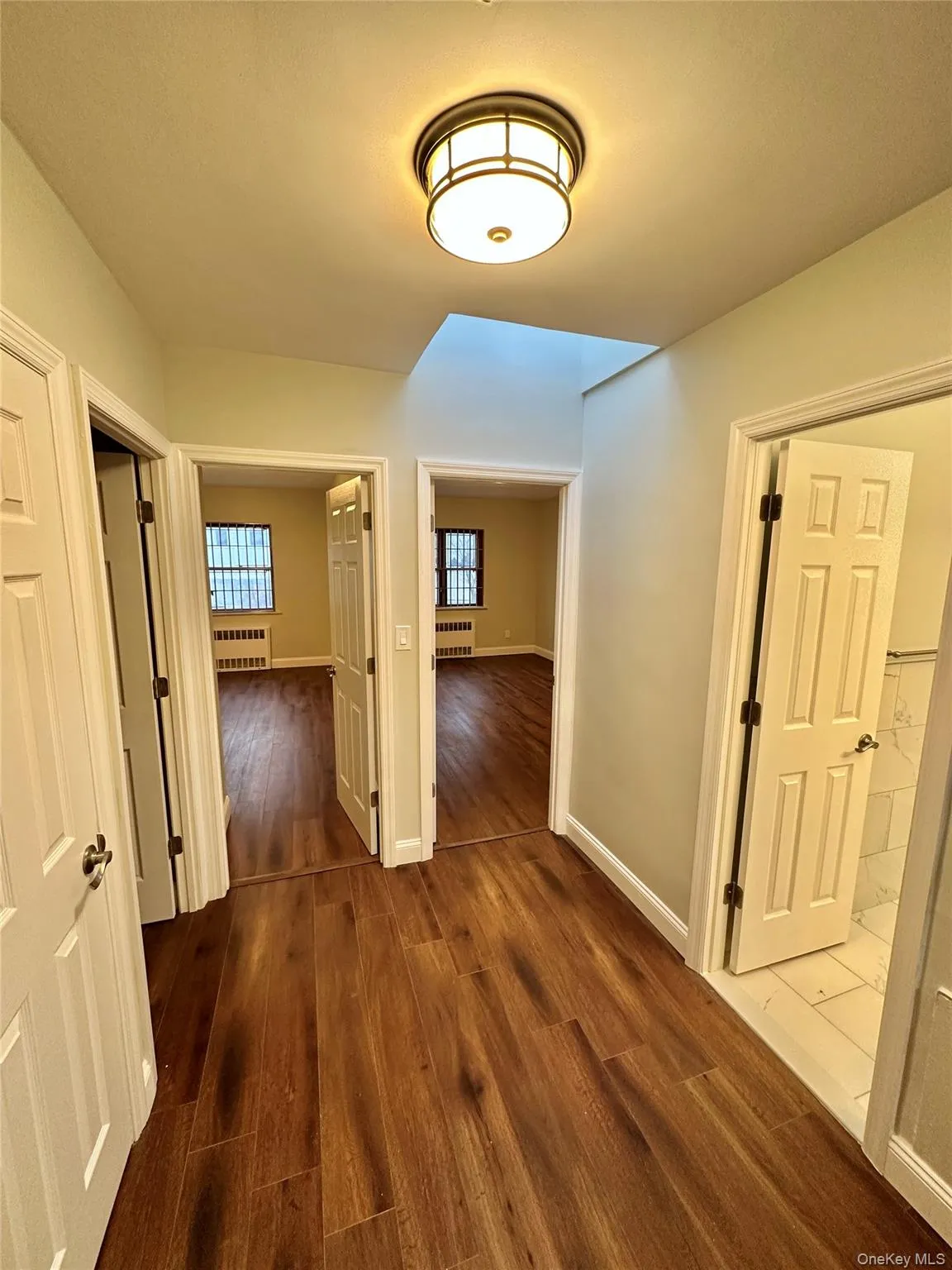Hallway featuring wood-finish flooring, a flush-mount ceiling light fixture, and light-toned wall paint Hallway featuring wood-finish flooring, a flush-mount ceiling light fixture, and light-toned wall paint