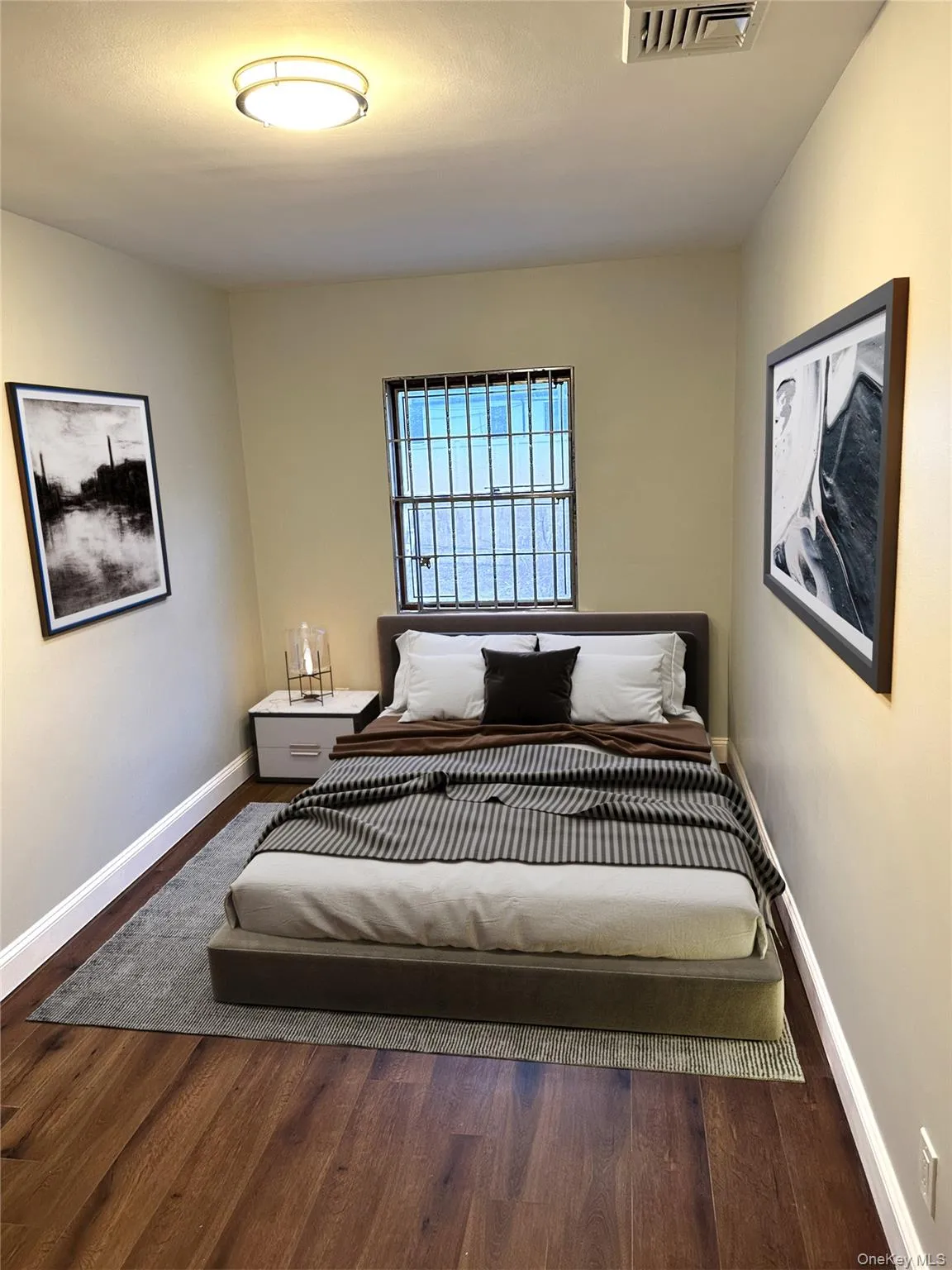 Bedroom featuring wood-finish flooring, a window with security bars, and a flush-mount ceiling light Bedroom featuring wood-finish flooring, a window with security bars, and a flush-mount ceiling light
