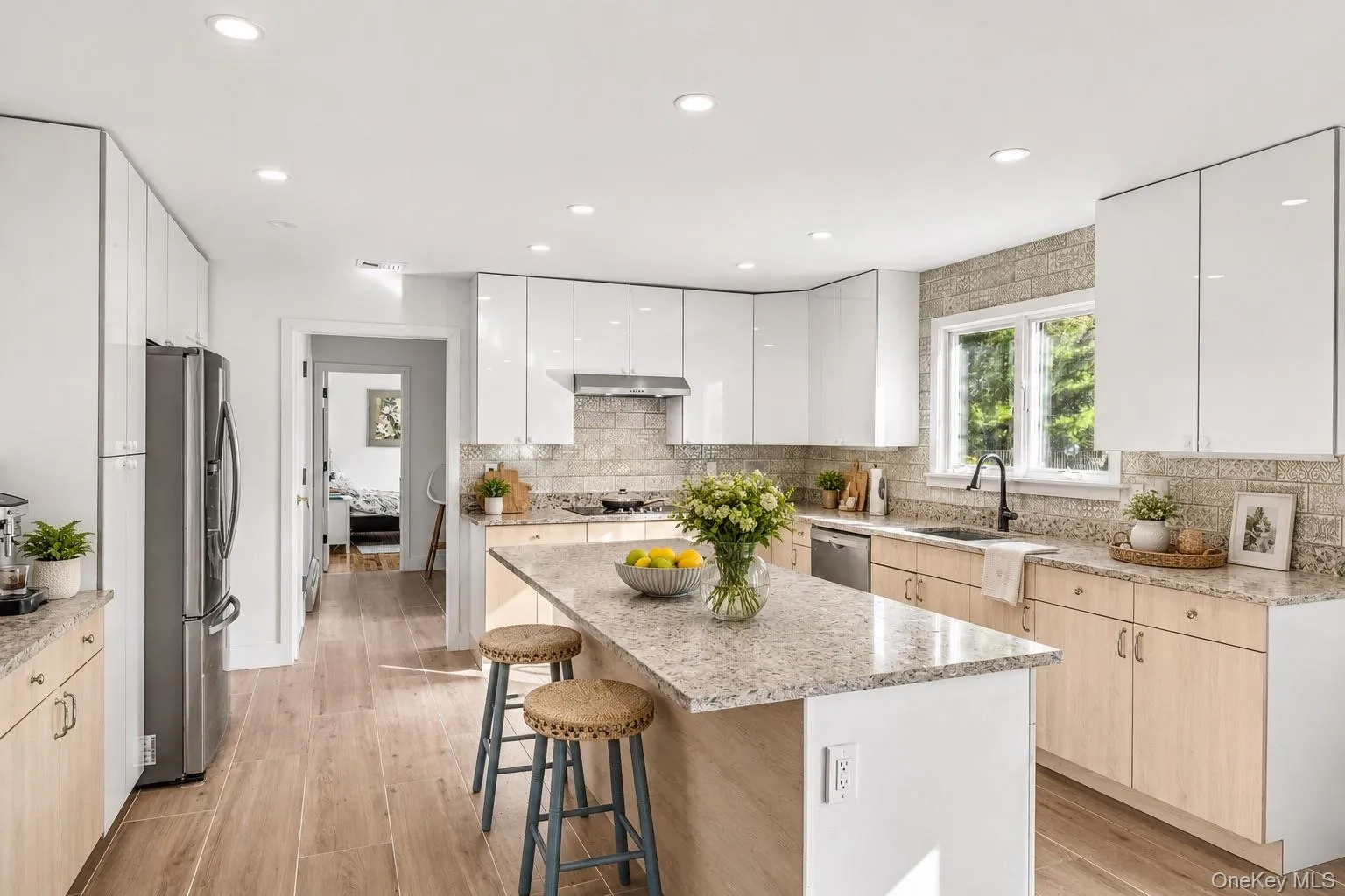 Kitchen featuring an island with stone countertops, stainless steel appliances, wood-finish flooring, light wood-tone base cabinetry, and sleek white upper cabinetry Kitchen featuring an island with stone countertops, stainless steel appliances, wood-finish flooring, light wood-tone base cabinetry, and sleek white upper cabinetry
