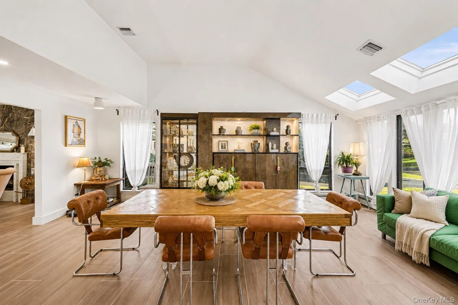 Vaulted ceiling dining area featuring two skylights, multiple large windows, wood-finish flooring, and a built-in display cabinet with integrated lighting Vaulted ceiling dining area featuring two skylights, multiple large windows, wood-finish flooring, and a built-in display cabinet with integrated lighting