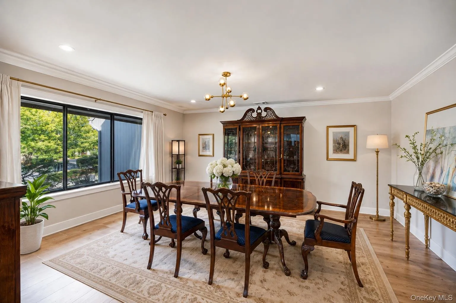 Dining room featuring a large picture window, wood-finish flooring, recessed lighting, crown molding, and a modern chandelier Dining room featuring a large picture window, wood-finish flooring, recessed lighting, crown molding, and a modern chandelier
