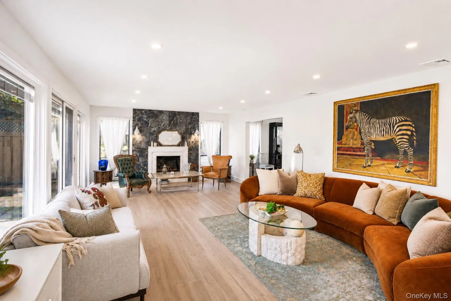 Bright living area featuring wood-finish flooring, recessed lighting, and a white fireplace with a dark stone accent wall Bright living area featuring wood-finish flooring, recessed lighting, and a white fireplace with a dark stone accent wall