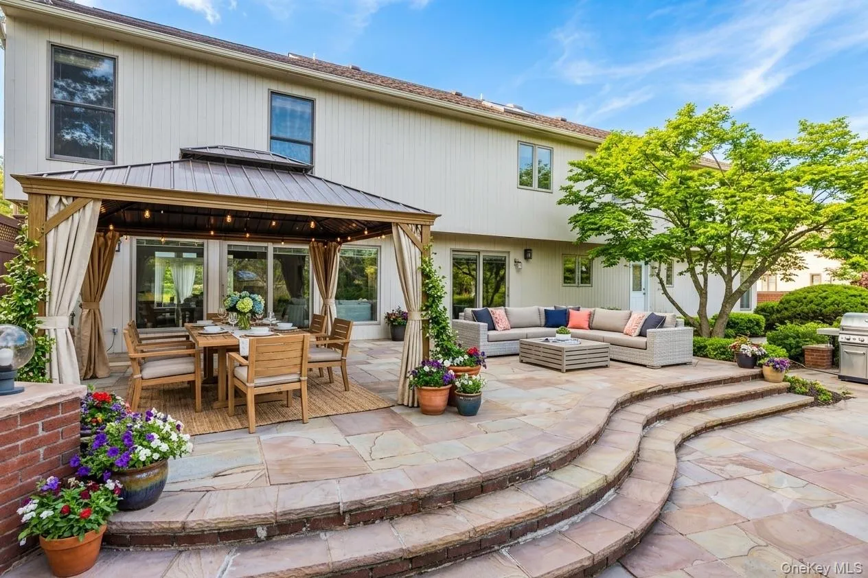Expansive flagstone patio featuring a covered dining area with privacy curtains, multiple seating zones, and a mature tree Expansive flagstone patio featuring a covered dining area with privacy curtains, multiple seating zones, and a mature tree