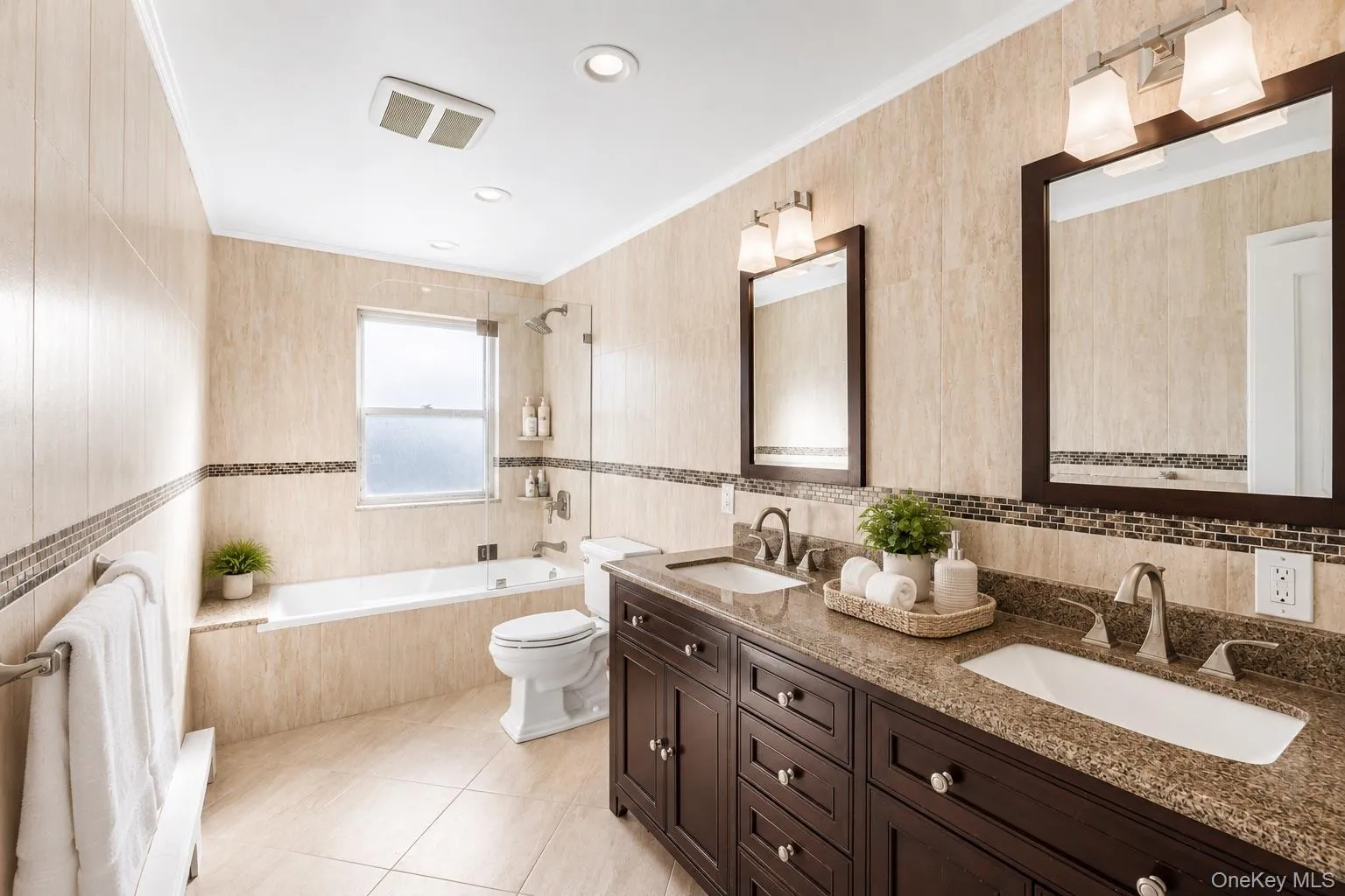 Bathroom featuring a double vanity with stone countertops, a built-in bathtub with a shower, and light-toned tile flooring and walls Bathroom featuring a double vanity with stone countertops, a built-in bathtub with a shower, and light-toned tile flooring and walls