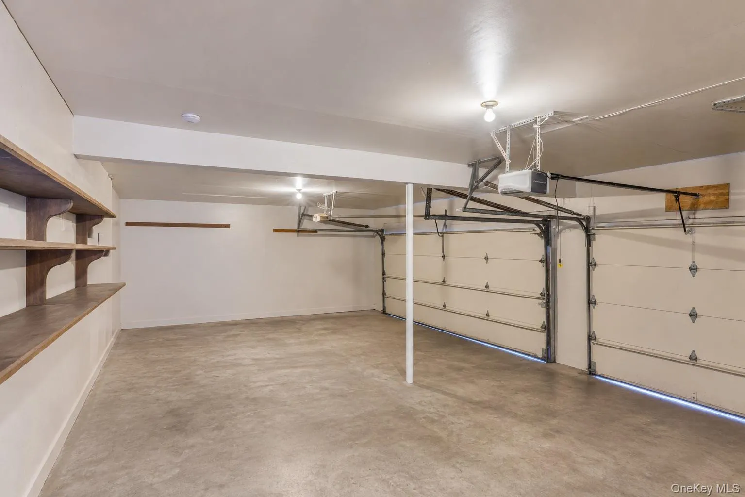 Spacious garage featuring a concrete floor, two overhead garage doors, automatic openers, built-in shelving, and overhead lighting Spacious garage featuring a concrete floor, two overhead garage doors, automatic openers, built-in shelving, and overhead lighting