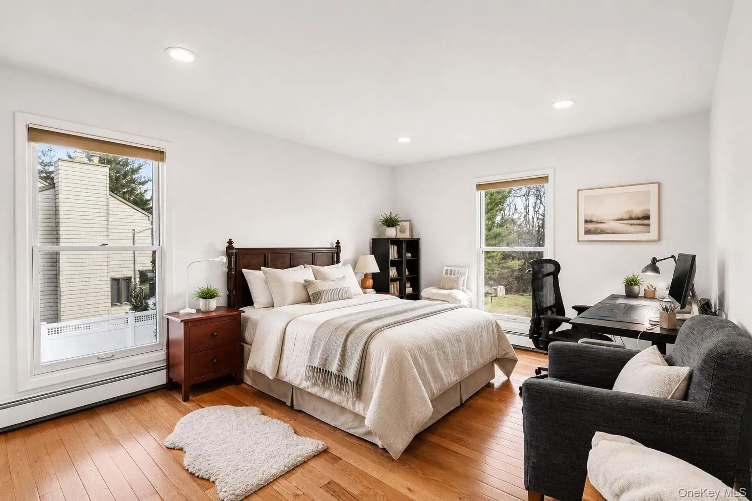 Bright bedroom featuring two large windows, recessed lighting, wood-finish flooring, a dark wood bed frame, and white walls Bright bedroom featuring two large windows, recessed lighting, wood-finish flooring, a dark wood bed frame, and white walls