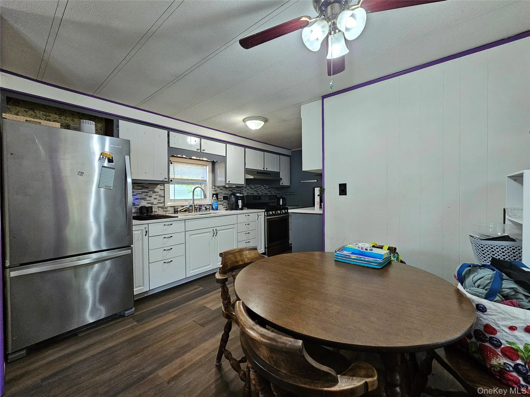 Kitchen featuring white cabinetry, a stainless steel refrigerator, dark wood-finish flooring, and a tiled backsplash Kitchen featuring white cabinetry, a stainless steel refrigerator, dark wood-finish flooring, and a tiled backsplash