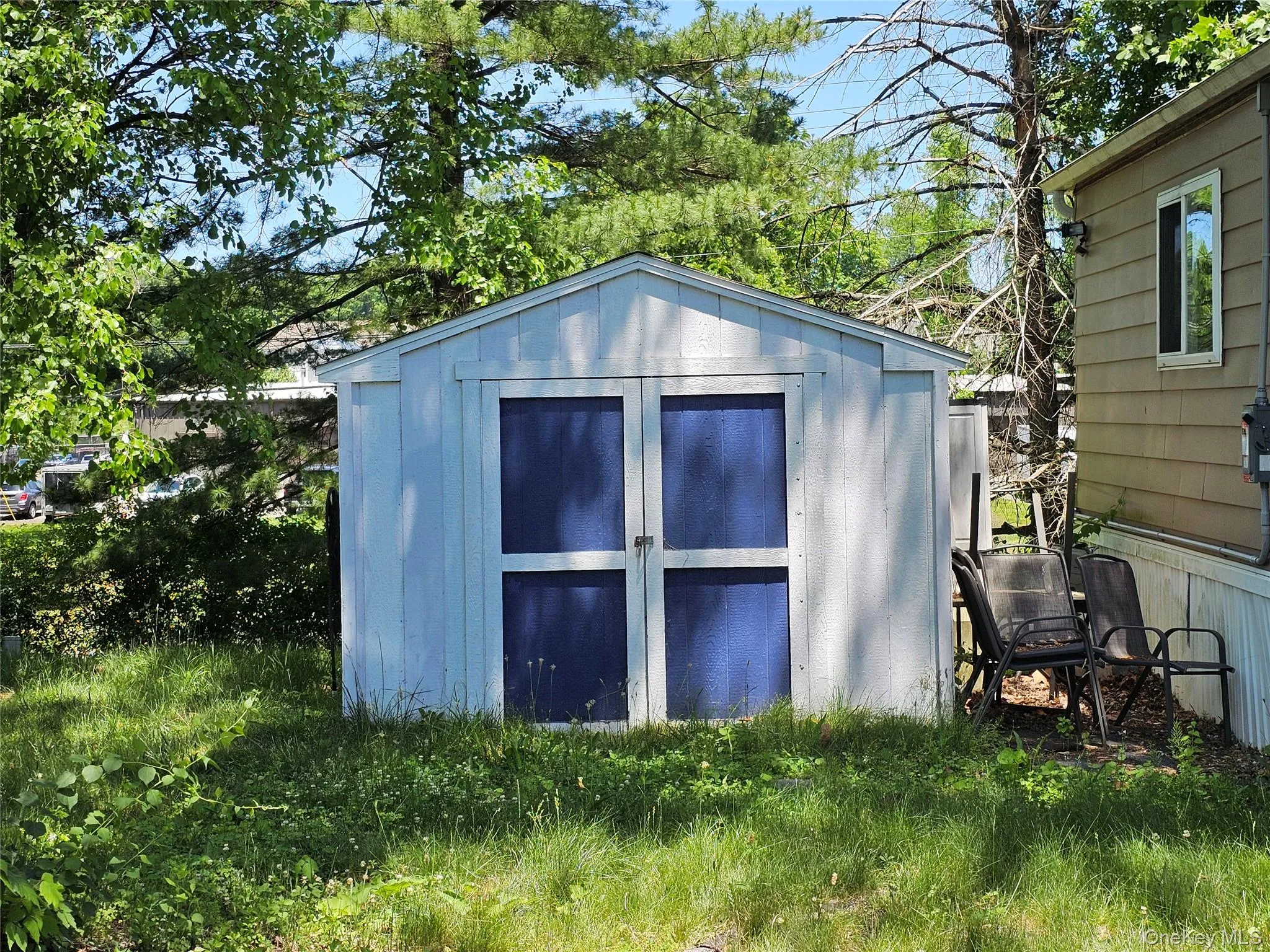Gable-roof storage shed with light-colored siding and blue-painted double doors Gable-roof storage shed with light-colored siding and blue-painted double doors