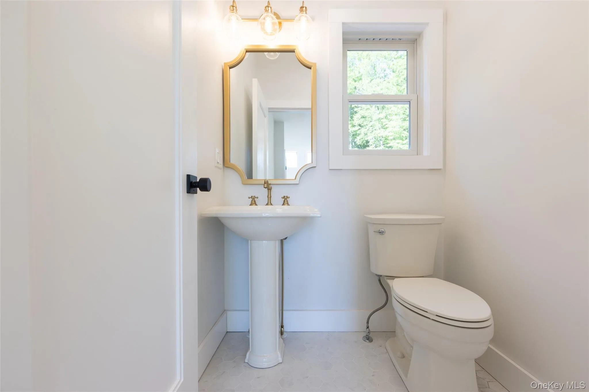 Pedestal sink with brass-finish faucet, framed mirror, and coordinating lighting fixture Pedestal sink with brass-finish faucet, framed mirror, and coordinating lighting fixture