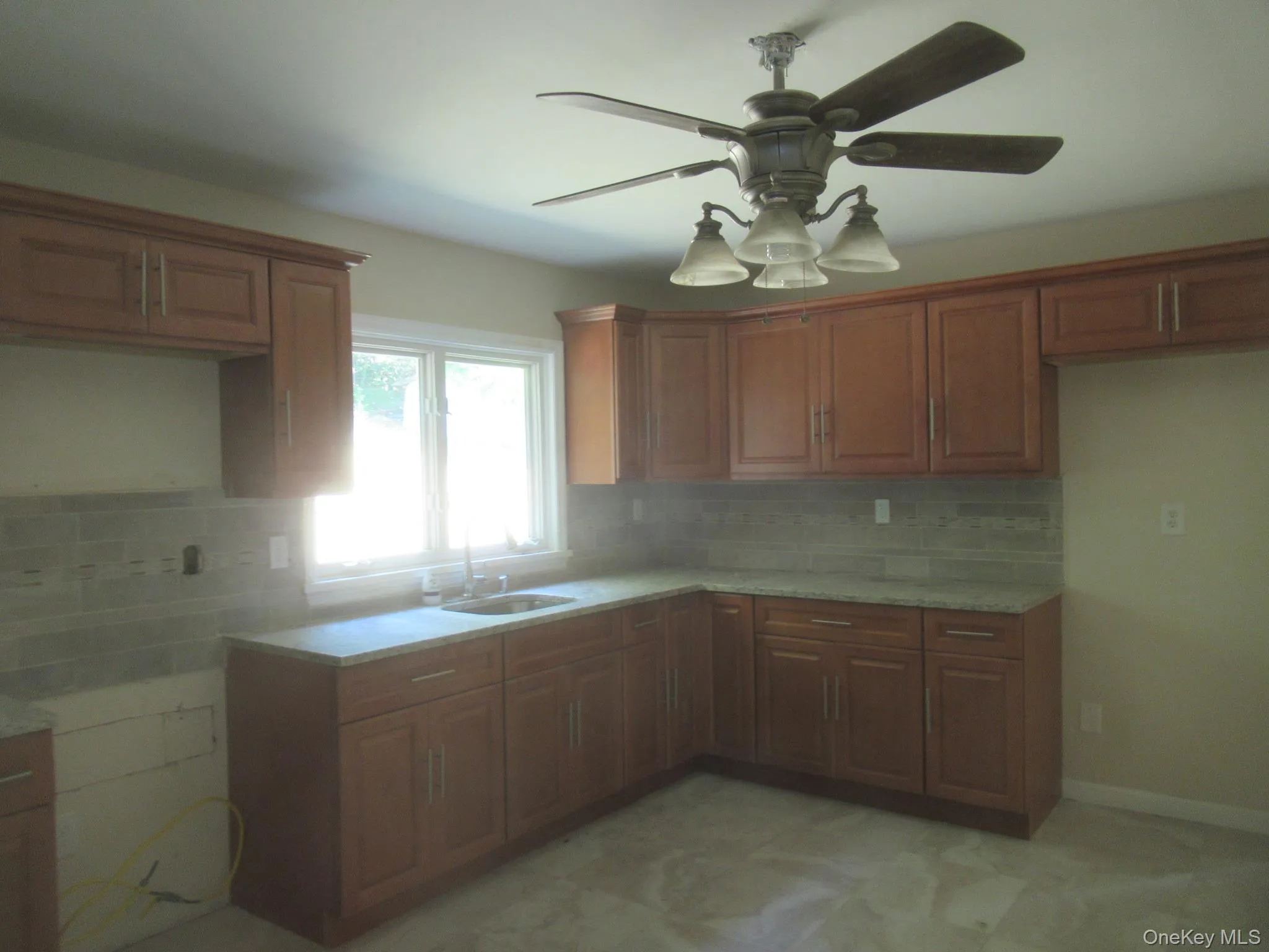 Kitchen with brown cabinets, tasteful backsplash, a ceiling fan, and light stone counters Kitchen with brown cabinets, tasteful backsplash, a ceiling fan, and light stone counters