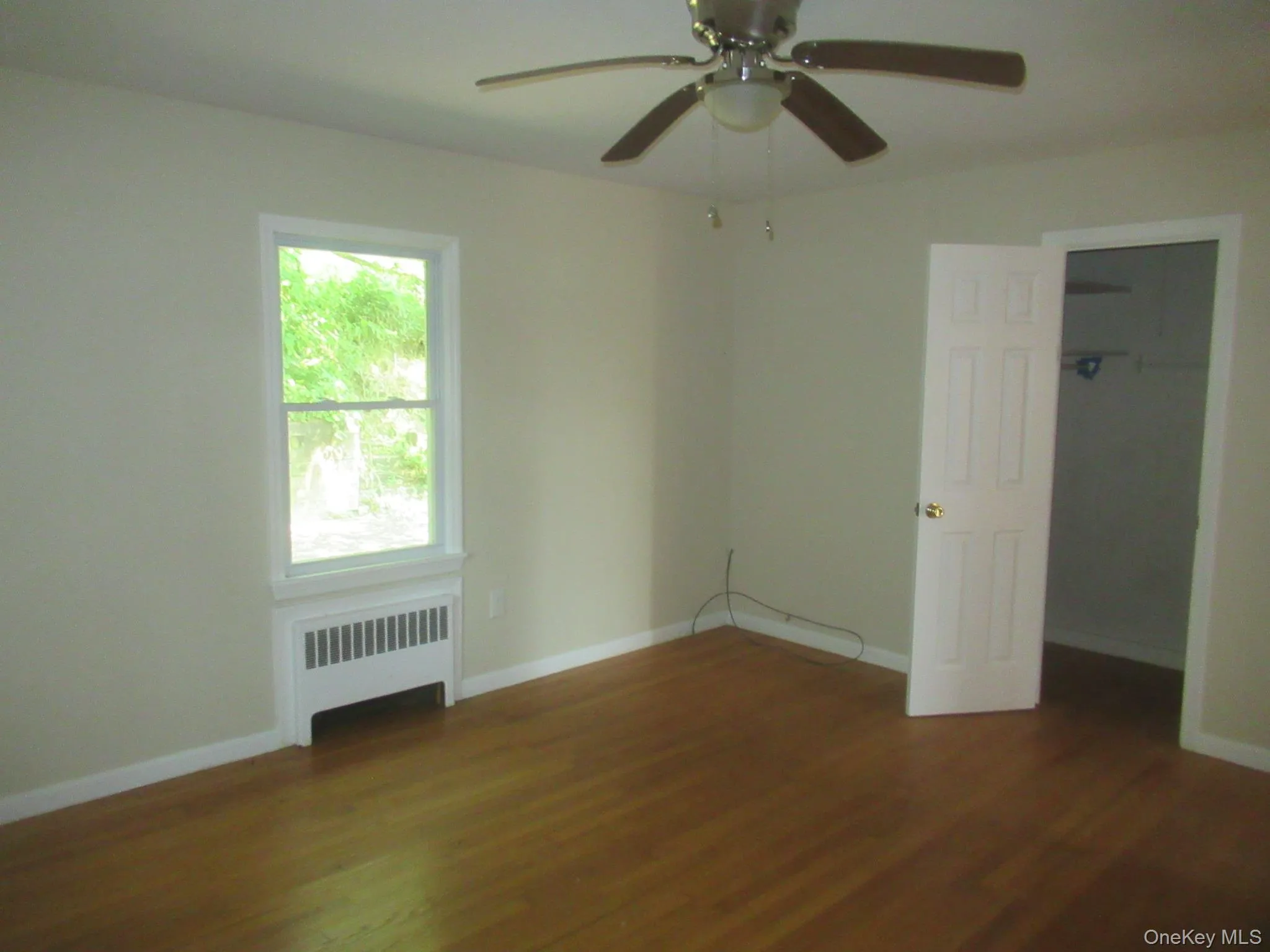 Unfurnished bedroom with radiator, dark wood-type flooring, and ceiling fan Unfurnished bedroom with radiator, dark wood-type flooring, and ceiling fan