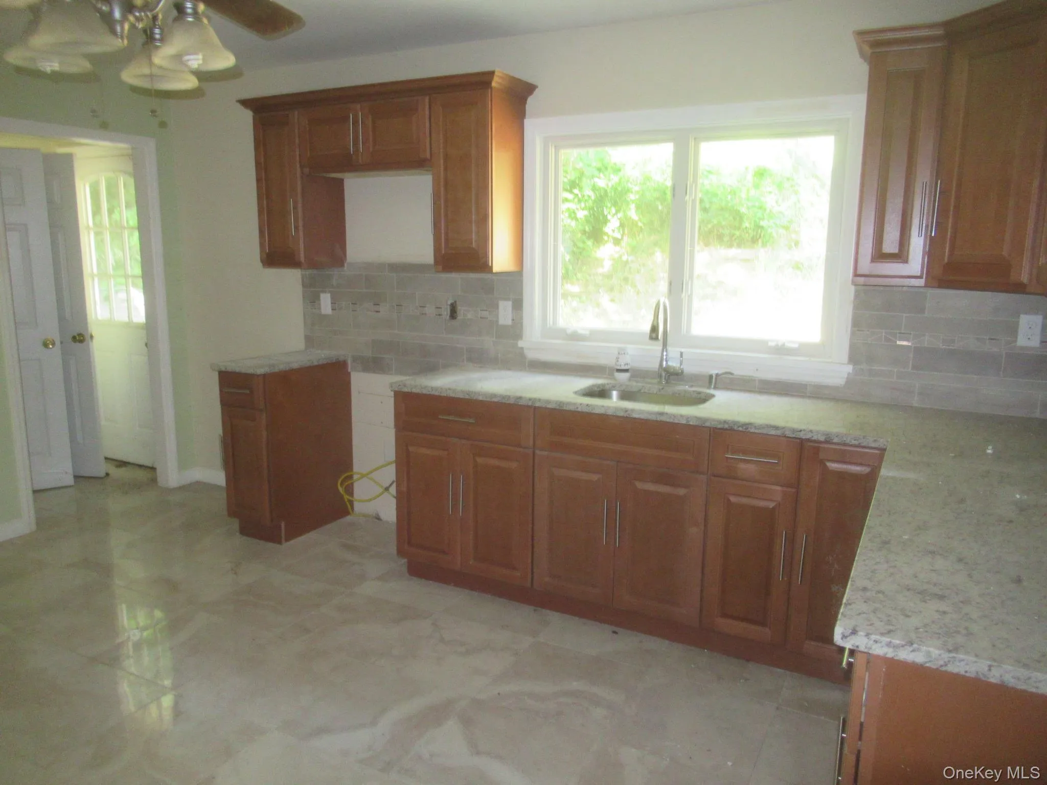 Kitchen featuring brown cabinets, backsplash, light stone countertops, and a ceiling fan Kitchen featuring brown cabinets, backsplash, light stone countertops, and a ceiling fan