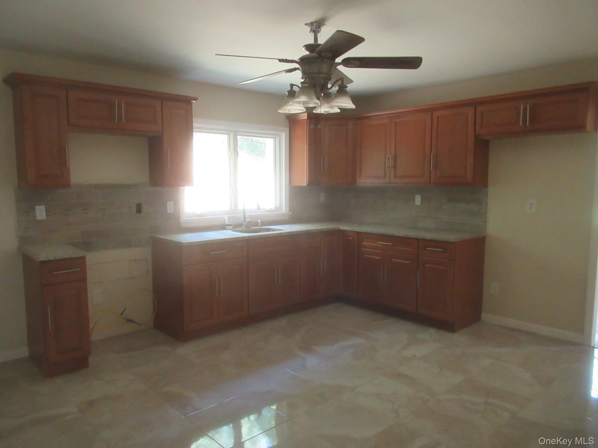 Kitchen with brown cabinetry, backsplash, and ceiling fan Kitchen with brown cabinetry, backsplash, and ceiling fan