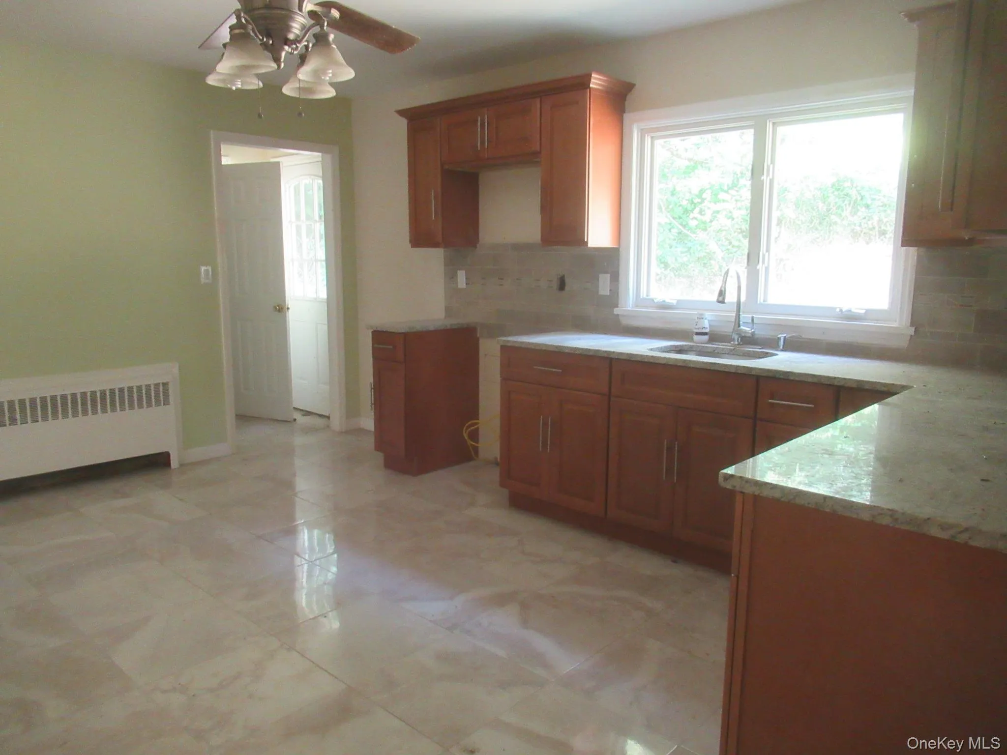 Kitchen with brown cabinetry, tasteful backsplash, healthy amount of natural light, and radiator Kitchen with brown cabinetry, tasteful backsplash, healthy amount of natural light, and radiator