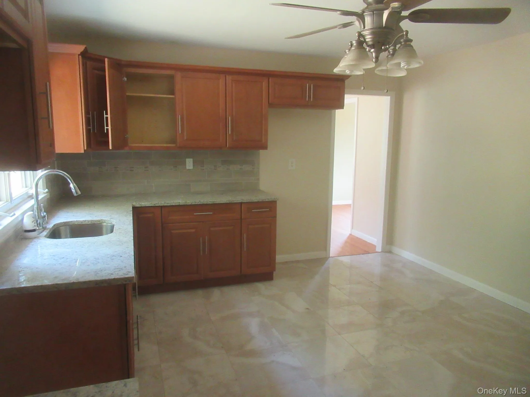 Kitchen featuring light stone countertops, brown cabinets, decorative backsplash, ceiling fan, and open shelves Kitchen featuring light stone countertops, brown cabinets, decorative backsplash, ceiling fan, and open shelves