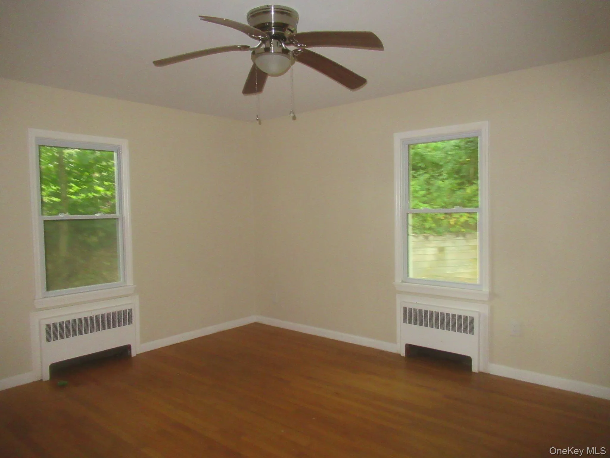 Unfurnished room featuring dark wood-style floors, radiator heating unit, and a ceiling fan Unfurnished room featuring dark wood-style floors, radiator heating unit, and a ceiling fan