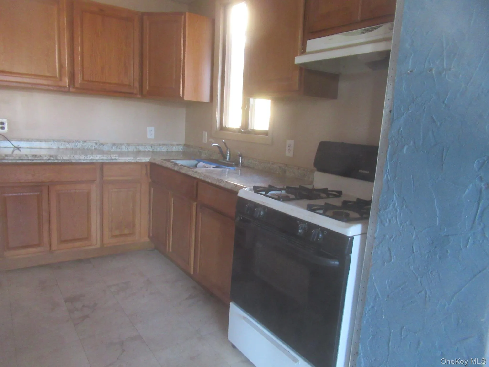Kitchen with white range with gas cooktop, under cabinet range hood, and brown cabinets Kitchen with white range with gas cooktop, under cabinet range hood, and brown cabinets