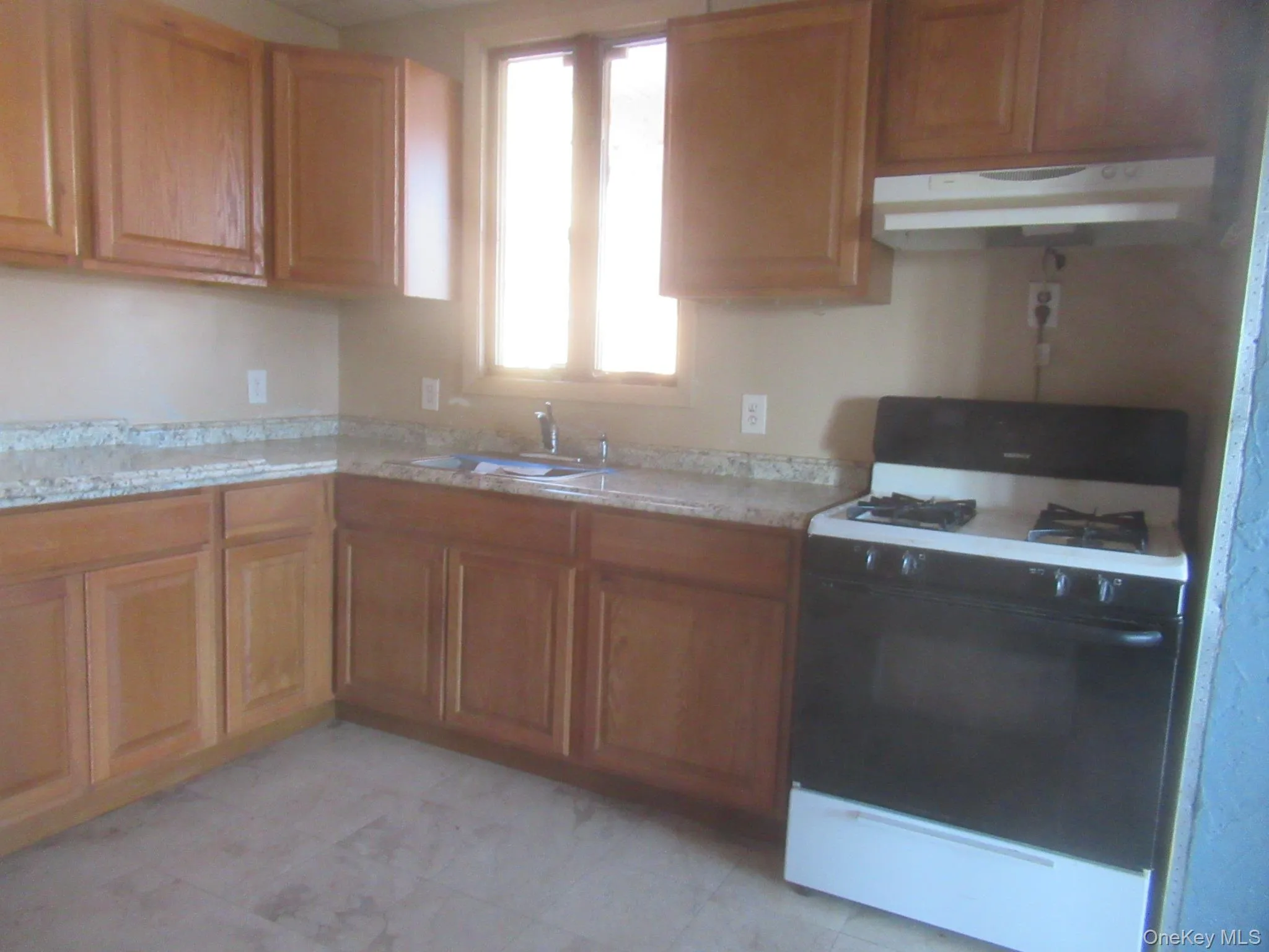 Kitchen with range with gas cooktop, brown cabinets, under cabinet range hood, and light stone countertops Kitchen with range with gas cooktop, brown cabinets, under cabinet range hood, and light stone countertops