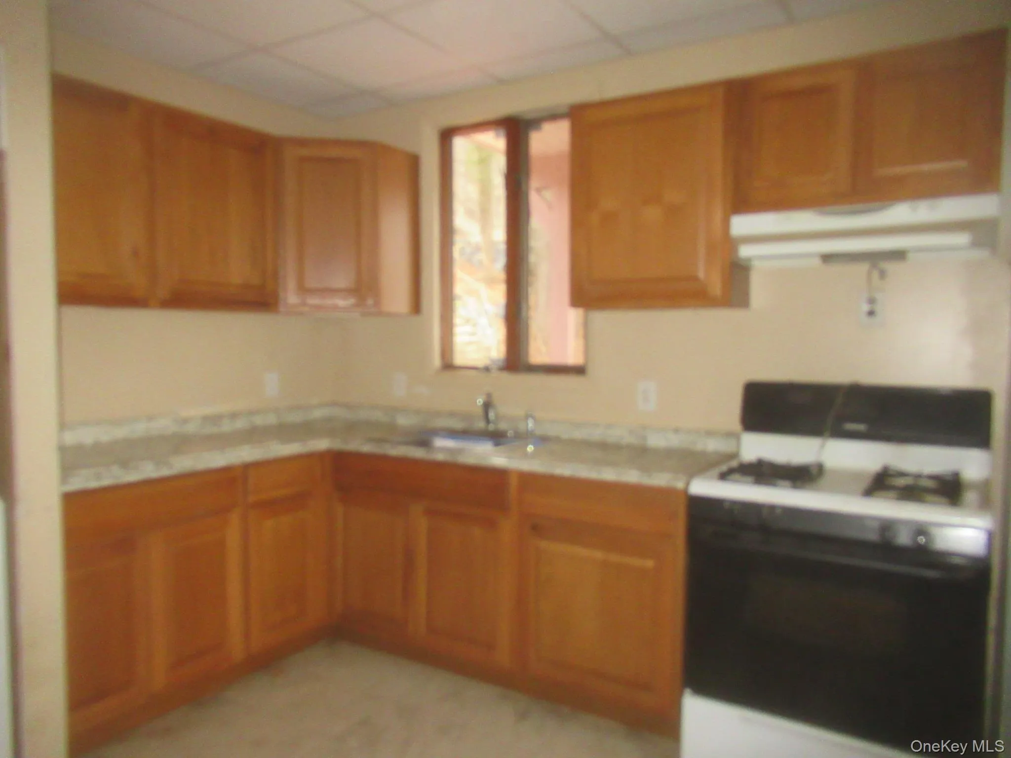Kitchen with gas range gas stove, under cabinet range hood, brown cabinetry, and a paneled ceiling Kitchen with gas range gas stove, under cabinet range hood, brown cabinetry, and a paneled ceiling