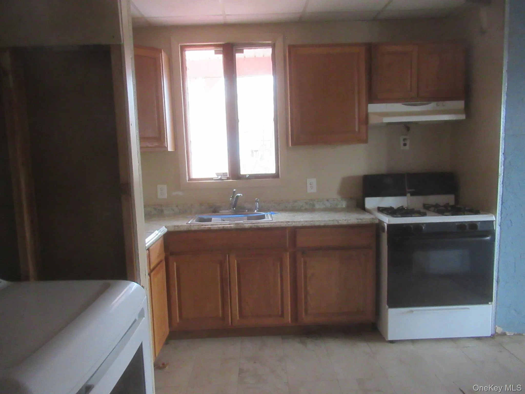Kitchen with white range with gas cooktop, brown cabinets, light countertops, and under cabinet range hood Kitchen with white range with gas cooktop, brown cabinets, light countertops, and under cabinet range hood