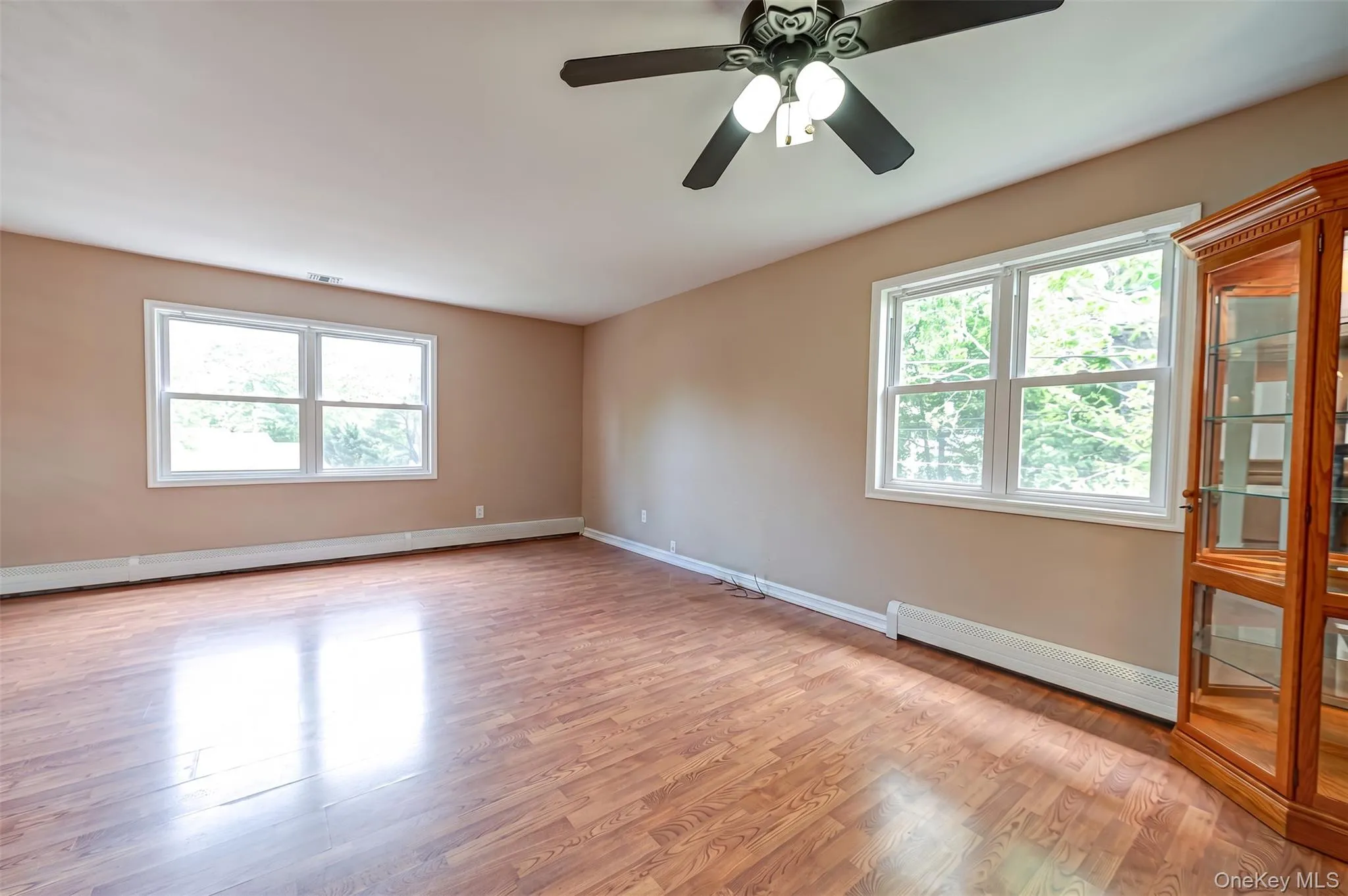Spacious room featuring wood-finish flooring, two large windows, and a ceiling fan with integrated lighting Spacious room featuring wood-finish flooring, two large windows, and a ceiling fan with integrated lighting