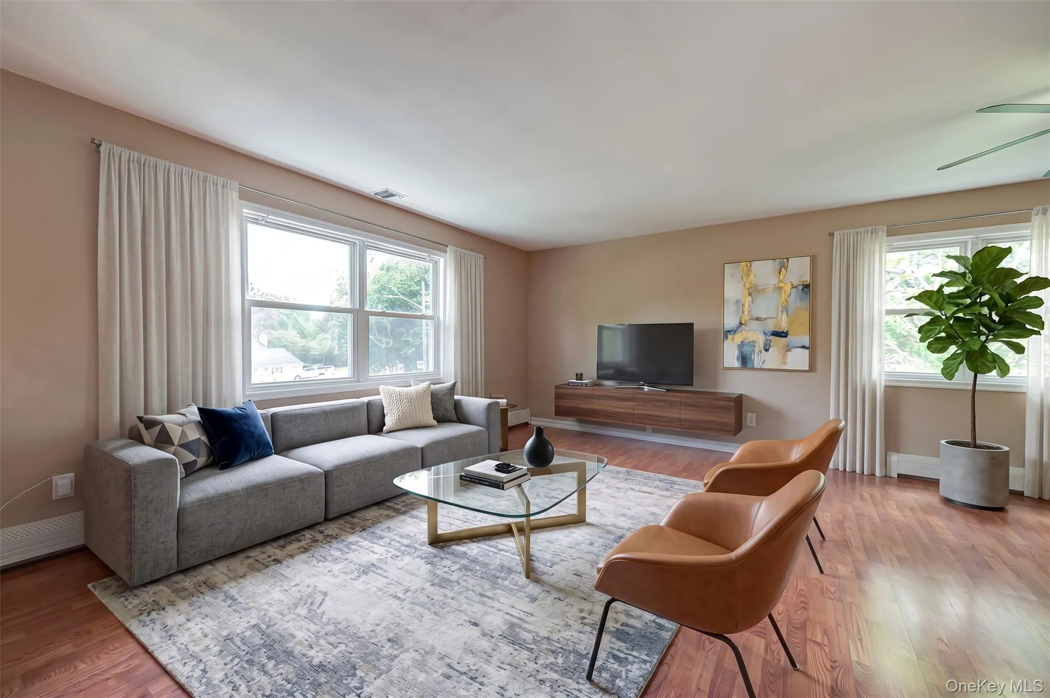 Expansive living area featuring wood-finish flooring, light-toned wall paint, and multiple large windows Expansive living area featuring wood-finish flooring, light-toned wall paint, and multiple large windows