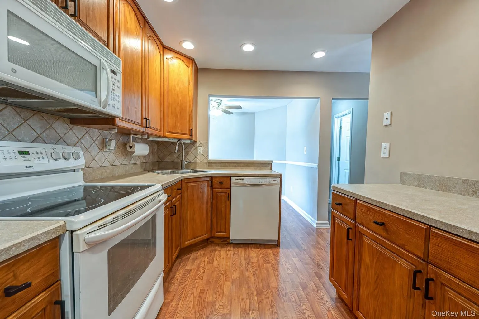 Kitchen featuring wood-finish flooring, wood cabinetry, white appliances, recessed lighting, and a neutral tile backsplash Kitchen featuring wood-finish flooring, wood cabinetry, white appliances, recessed lighting, and a neutral tile backsplash