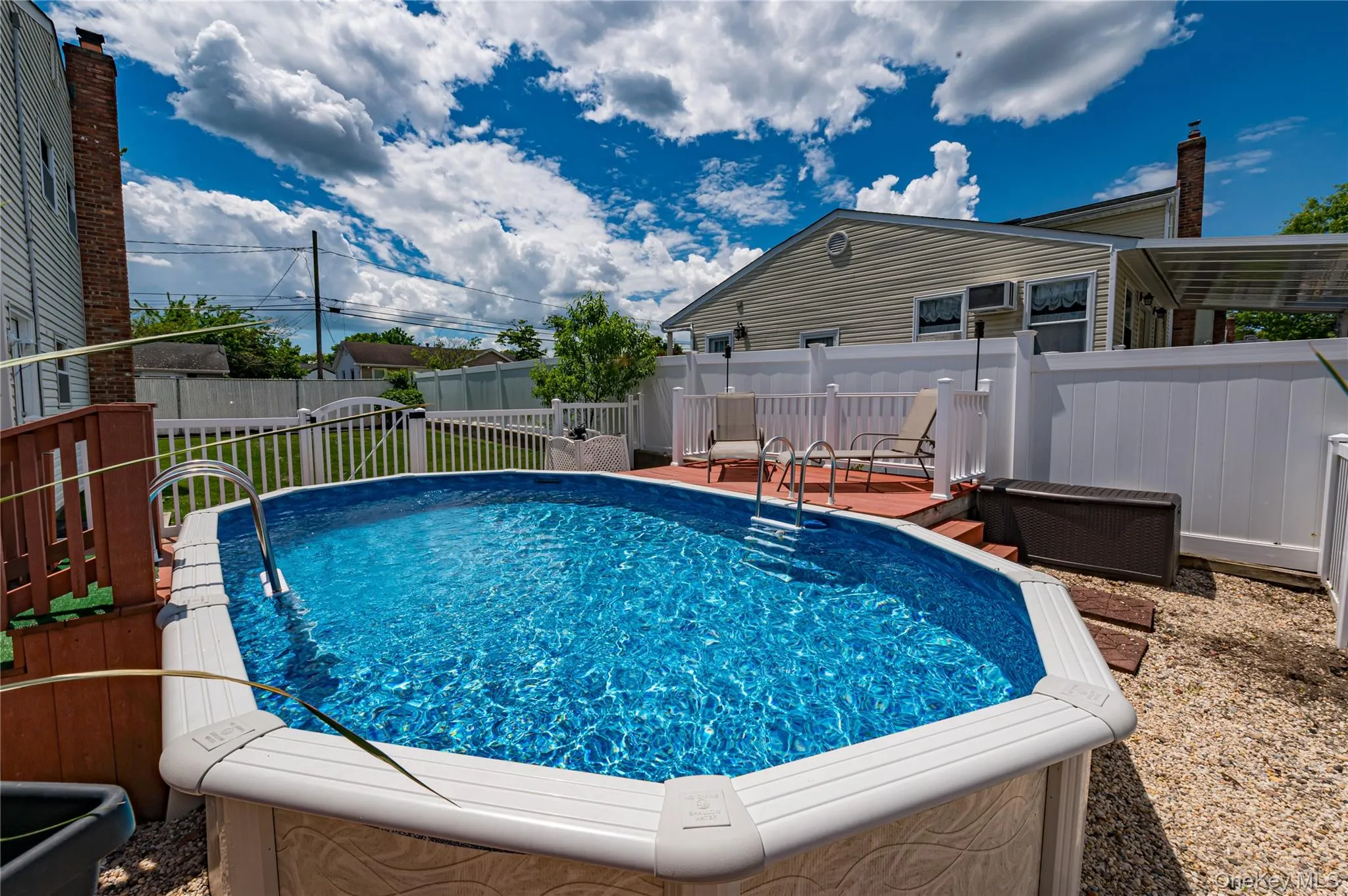 Above-ground swimming pool with integrated steps, surrounded by a wood-finish deck and white vinyl fencing Above-ground swimming pool with integrated steps, surrounded by a wood-finish deck and white vinyl fencing
