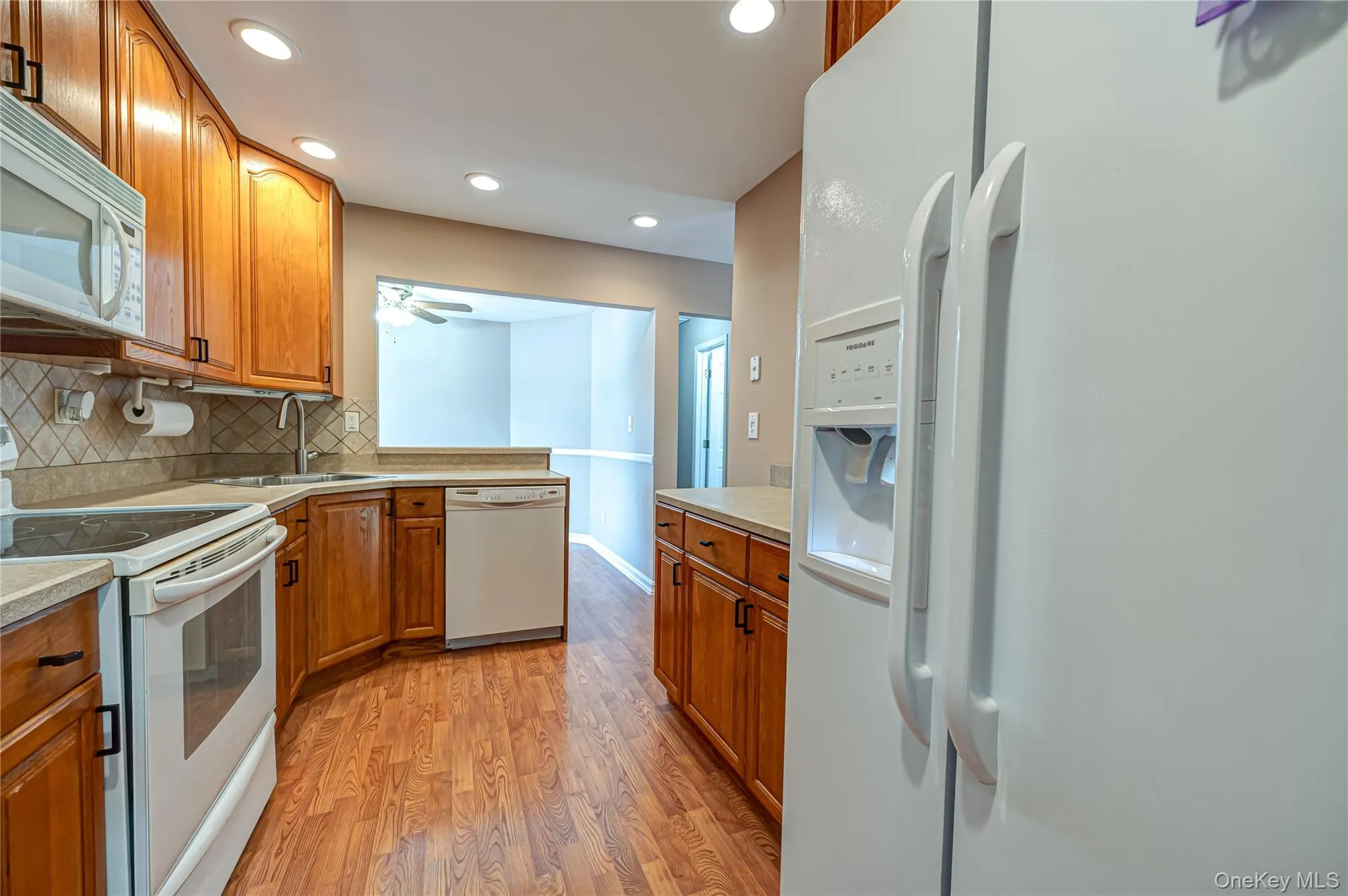 Well-appointed kitchen featuring wood-finish flooring, ample wood cabinetry, light-toned countertops, and a white appliance suite including a built-in microwave and dishwasher Well-appointed kitchen featuring wood-finish flooring, ample wood cabinetry, light-toned countertops, and a white appliance suite including a built-in microwave and dishwasher