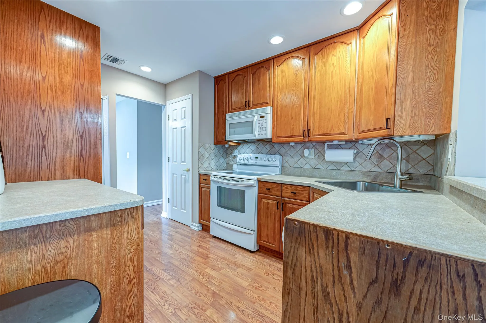Kitchen featuring wood-finish cabinetry, light-toned countertops, and a tile backsplash Kitchen featuring wood-finish cabinetry, light-toned countertops, and a tile backsplash