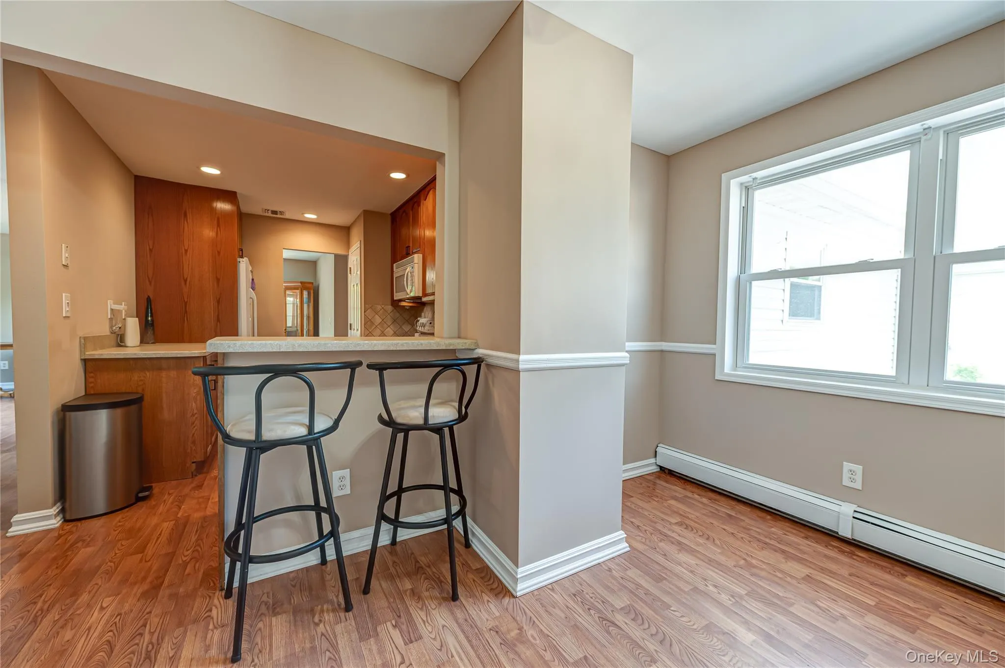 Kitchen bar seating area featuring wood-finish flooring, a light-colored countertop, recessed lighting, and a pass-through opening to the kitchen Kitchen bar seating area featuring wood-finish flooring, a light-colored countertop, recessed lighting, and a pass-through opening to the kitchen