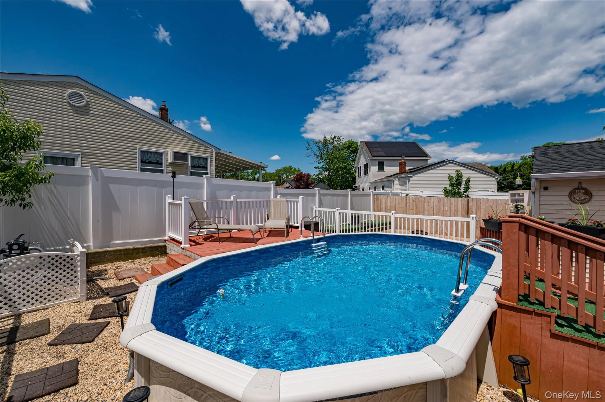 Above-ground swimming pool with surrounding wood-finish decking and white vinyl privacy fencing Above-ground swimming pool with surrounding wood-finish decking and white vinyl privacy fencing