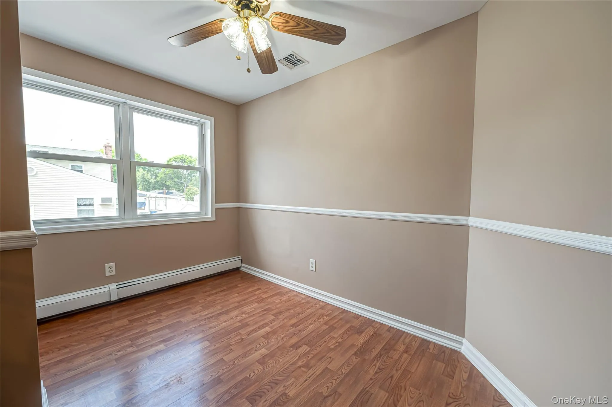 Room featuring wood-finish flooring, neutral-toned walls with chair rail molding, and a ceiling fan with integrated lighting Room featuring wood-finish flooring, neutral-toned walls with chair rail molding, and a ceiling fan with integrated lighting