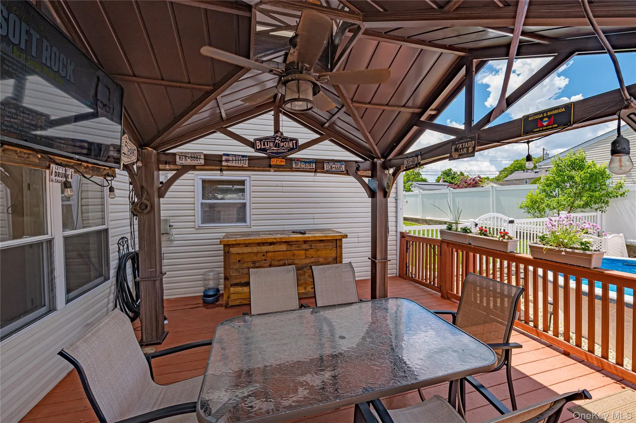 Covered outdoor deck with a ceiling fan, a built-in wooden bar, and a pool area beyond the railing Covered outdoor deck with a ceiling fan, a built-in wooden bar, and a pool area beyond the railing