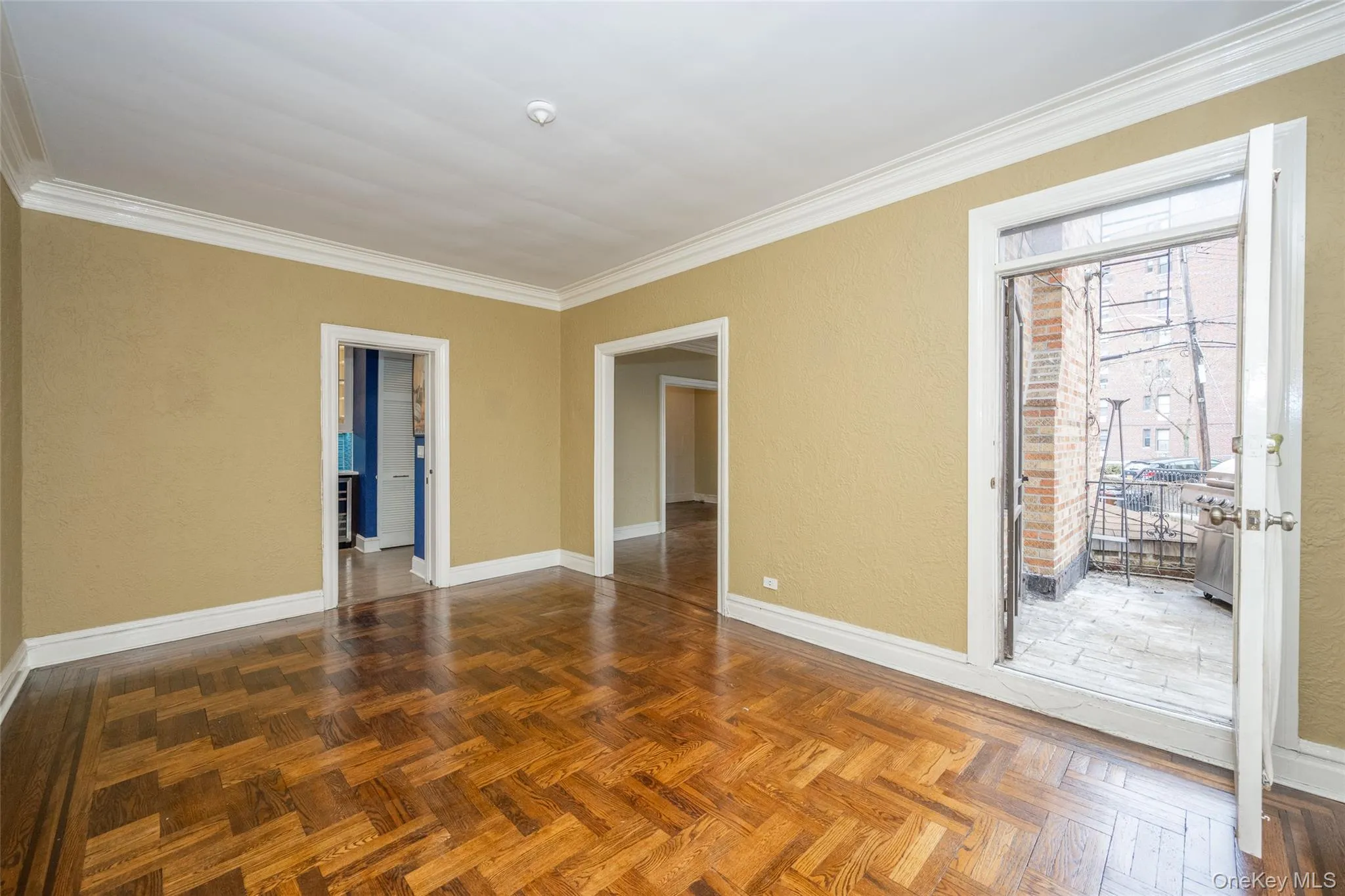 Living area featuring wood-finish herringbone flooring, crown molding, and a private outdoor balcony with stone-paved flooring Living area featuring wood-finish herringbone flooring, crown molding, and a private outdoor balcony with stone-paved flooring