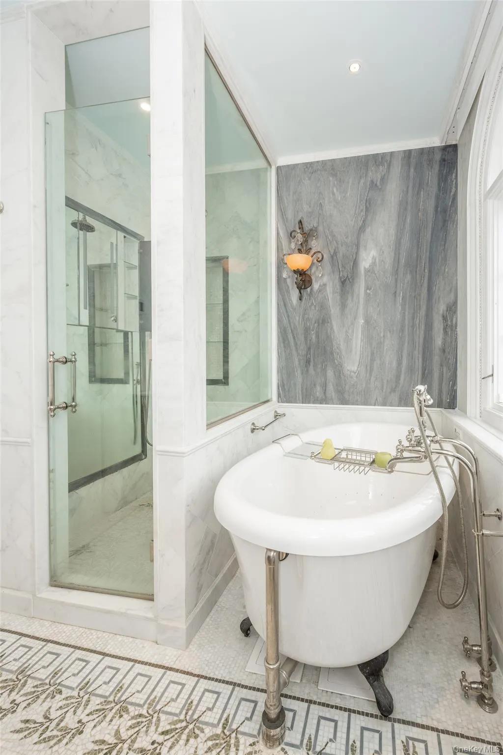 Bathroom featuring a clawfoot tub with floor-mounted fixtures, a glass-enclosed shower, marble wall paneling, and an ornate mosaic tile floor Bathroom featuring a clawfoot tub with floor-mounted fixtures, a glass-enclosed shower, marble wall paneling, and an ornate mosaic tile floor