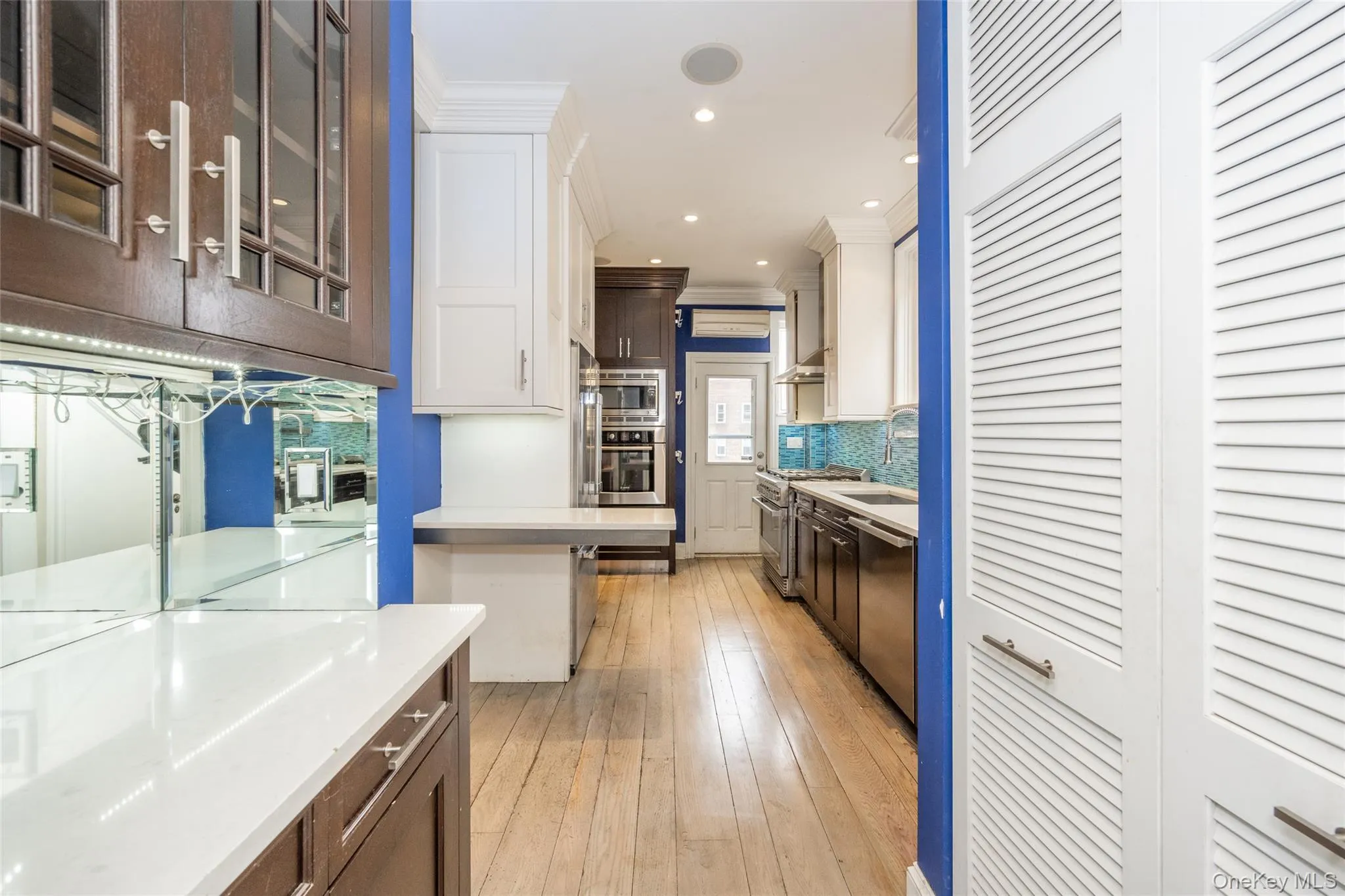 Galley kitchen featuring light wood-finish flooring, white countertops, and a mix of white and dark wood-finish cabinetry Galley kitchen featuring light wood-finish flooring, white countertops, and a mix of white and dark wood-finish cabinetry