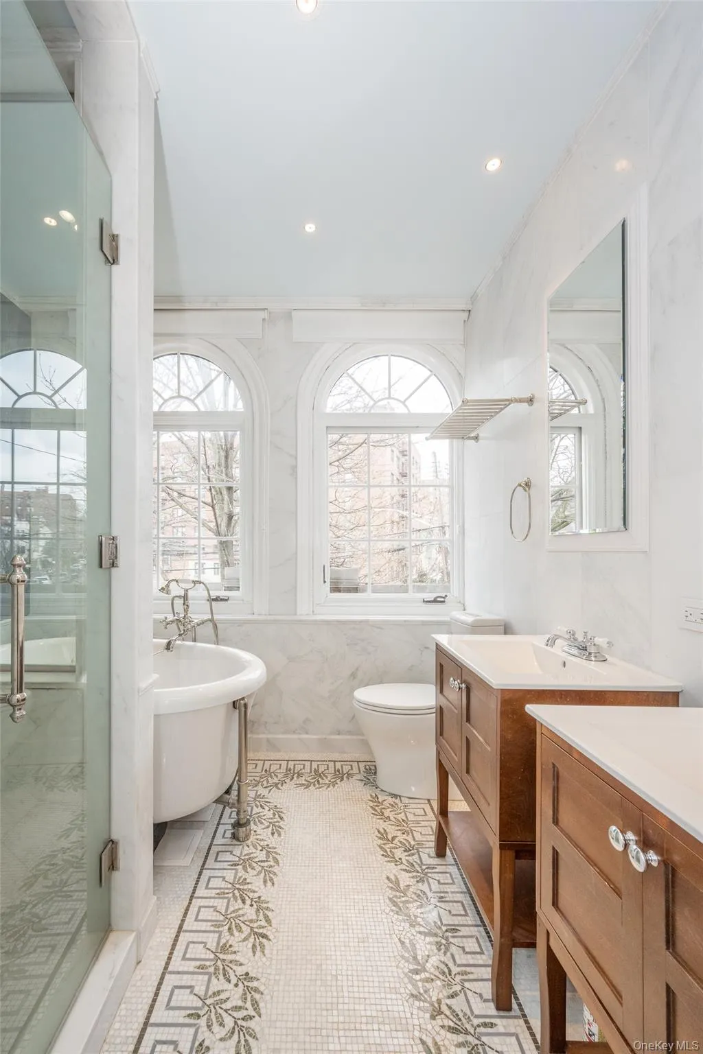 Bathroom featuring a glass-enclosed shower, freestanding clawfoot tub, and dual wood-finish vanities with integrated sinks Bathroom featuring a glass-enclosed shower, freestanding clawfoot tub, and dual wood-finish vanities with integrated sinks