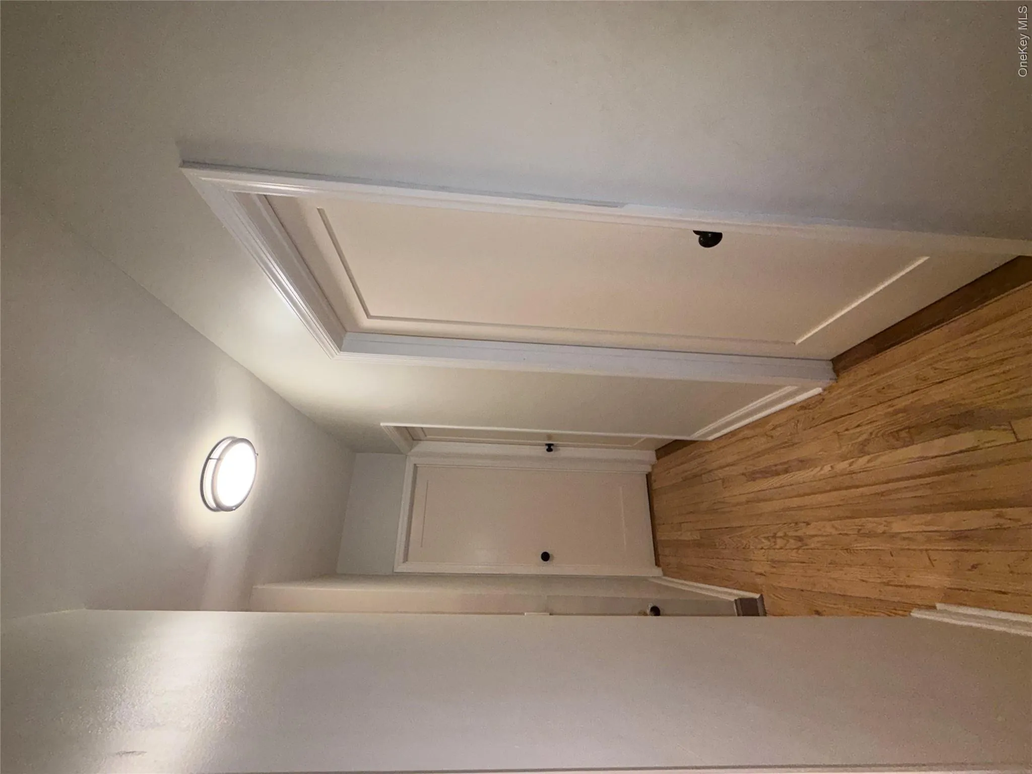 Hallway featuring wood-finish flooring, light-toned walls, multiple white doors with black hardware, and a modern flush-mount ceiling light Hallway featuring wood-finish flooring, light-toned walls, multiple white doors with black hardware, and a modern flush-mount ceiling light