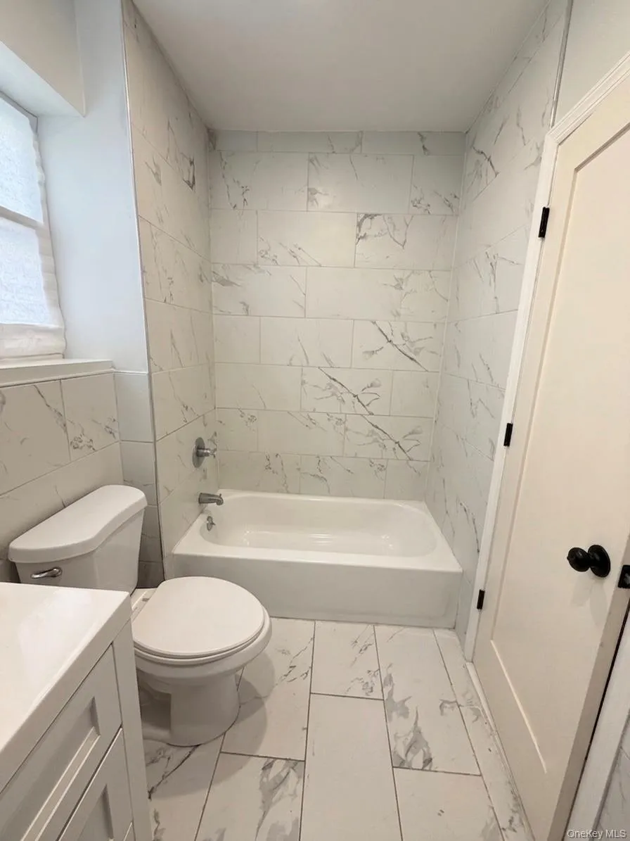 Bathroom featuring a white bathtub with chrome fixtures, marble-look tiled walls, and coordinating marble-look floor tiles Bathroom featuring a white bathtub with chrome fixtures, marble-look tiled walls, and coordinating marble-look floor tiles