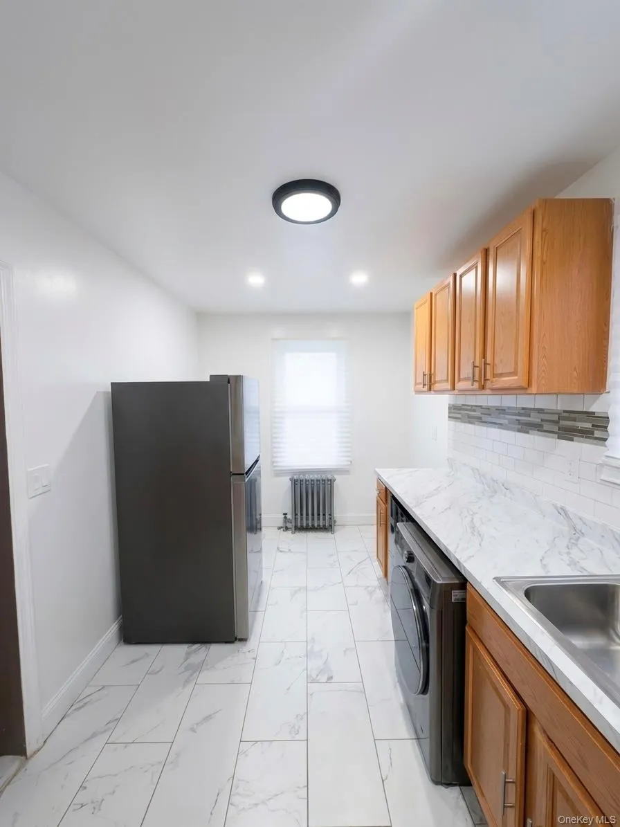 Kitchen featuring wood cabinetry, a stainless steel sink, and white marble-patterned tile flooring Kitchen featuring wood cabinetry, a stainless steel sink, and white marble-patterned tile flooring