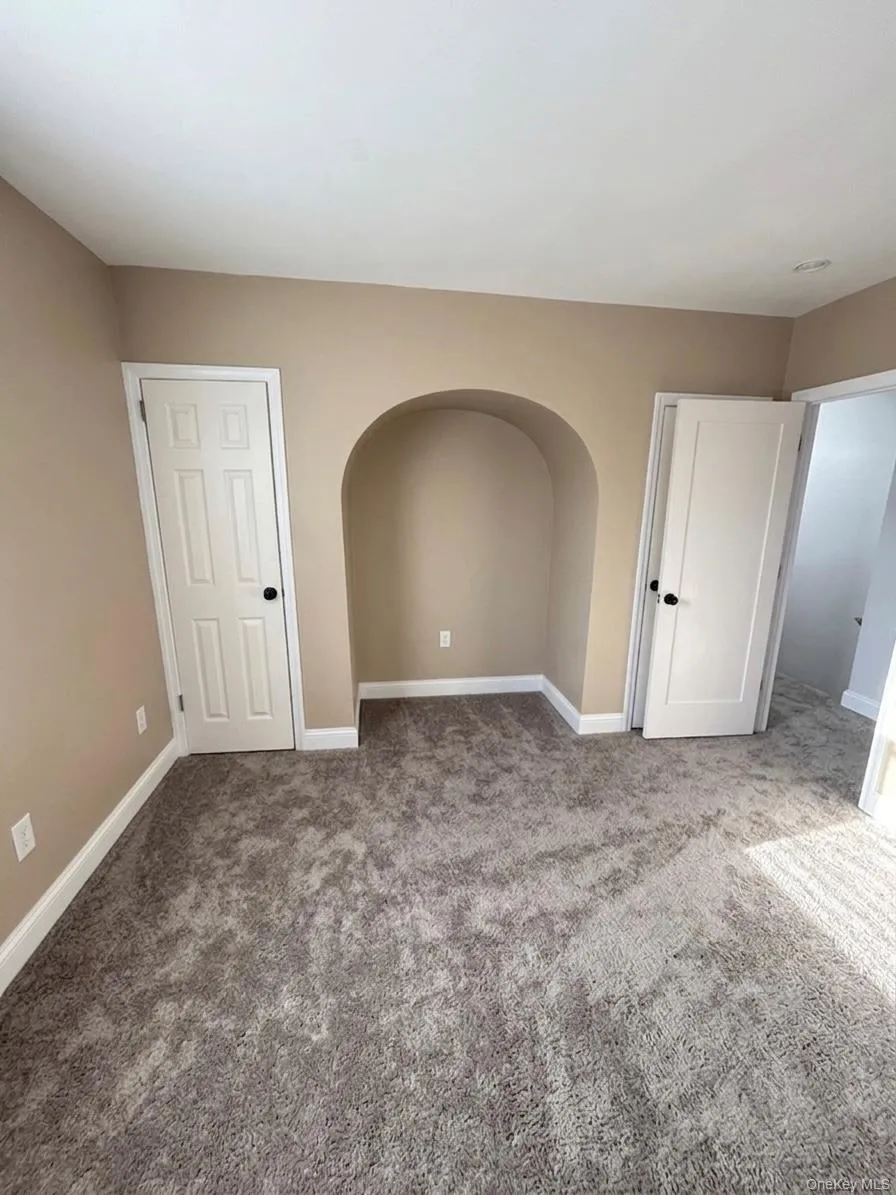 Neutral-toned room featuring an arched wall niche, plush gray carpeting, and white trim Neutral-toned room featuring an arched wall niche, plush gray carpeting, and white trim