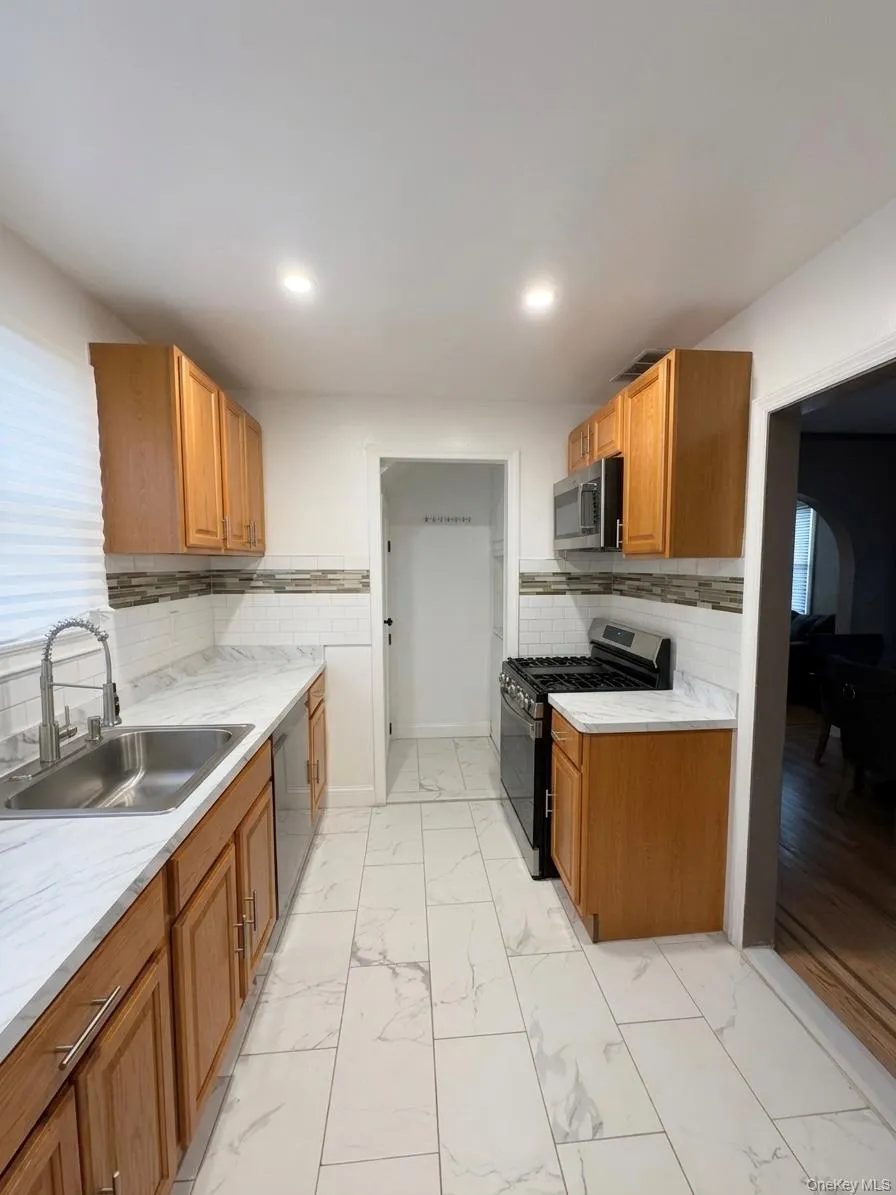 Galley kitchen featuring wood cabinetry, stainless steel appliances, and wood-finish flooring Galley kitchen featuring wood cabinetry, stainless steel appliances, and wood-finish flooring
