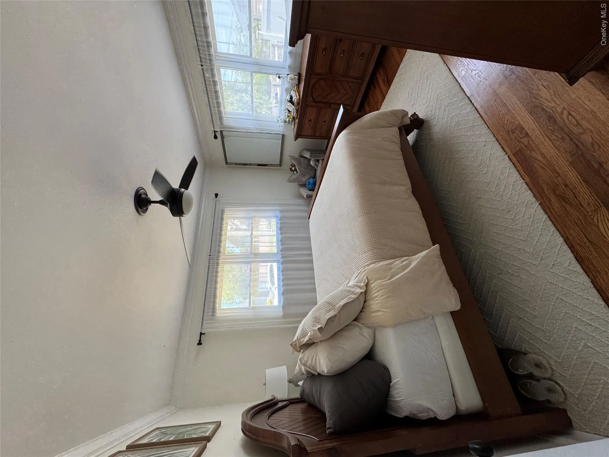 Bright sunlit bedroom room featuring two windows, crown molding, wood-finish flooring, and a ceiling fan Bright sunlit bedroom room featuring two windows, crown molding, wood-finish flooring, and a ceiling fan