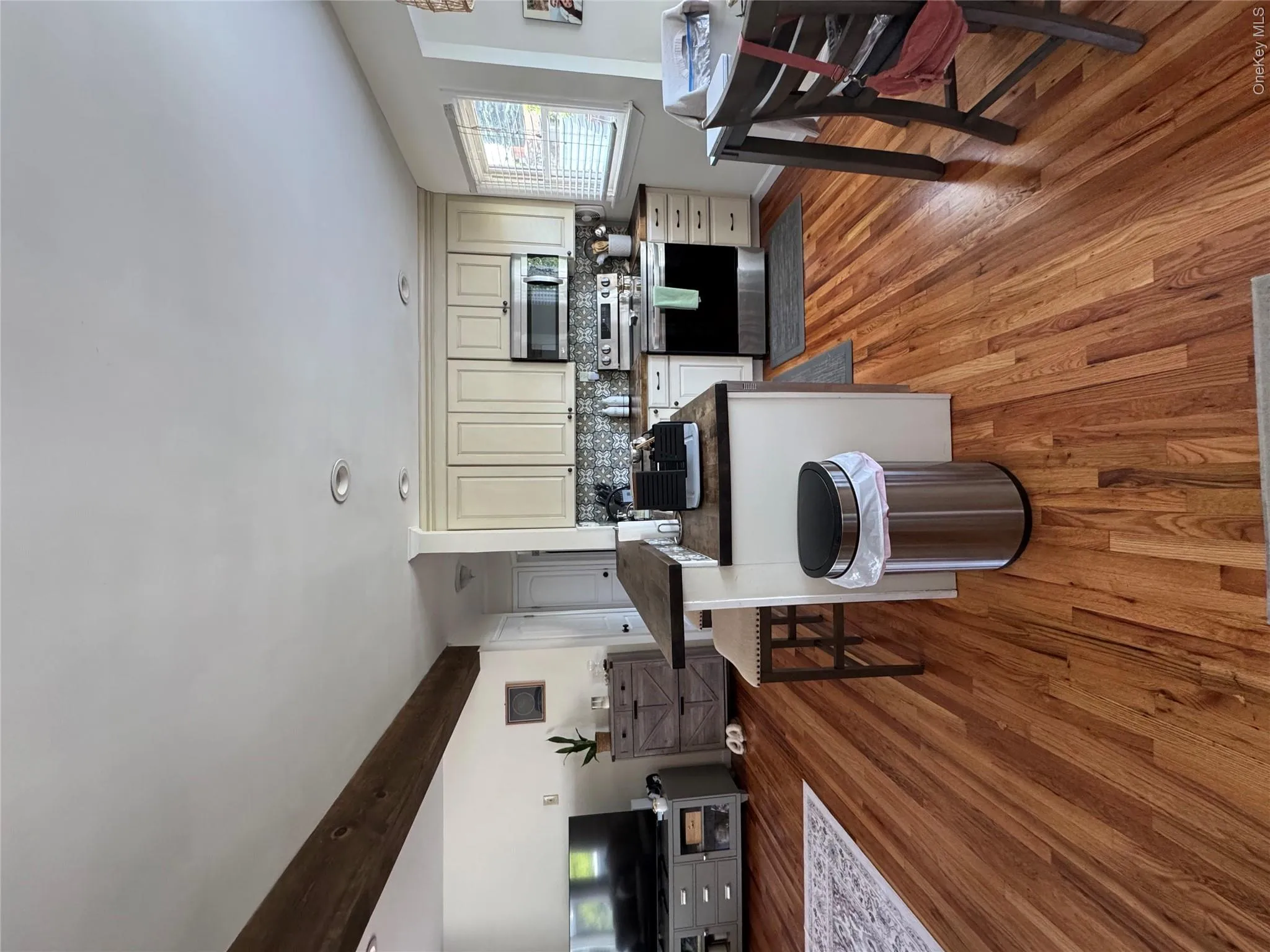 Kitchen featuring wood-finish flooring, light-toned cabinetry, stainless steel appliances, and a patterned tile backsplash Kitchen featuring wood-finish flooring, light-toned cabinetry, stainless steel appliances, and a patterned tile backsplash