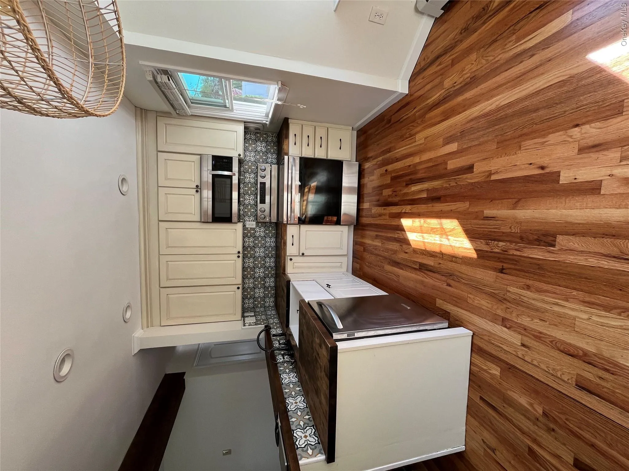 Kitchen featuring wood-finish flooring, cream-toned cabinetry with dark hardware, stainless steel appliances, and patterned tile backsplash Kitchen featuring wood-finish flooring, cream-toned cabinetry with dark hardware, stainless steel appliances, and patterned tile backsplash