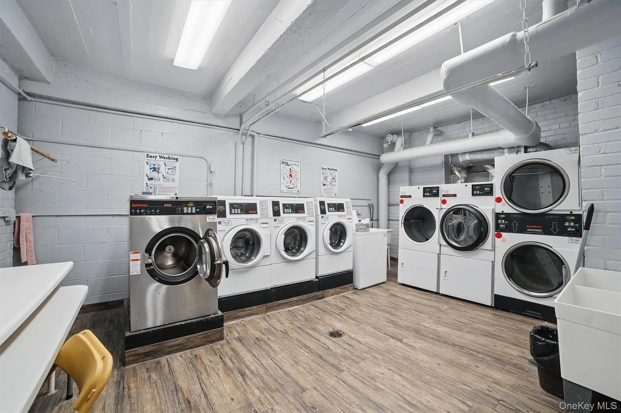 Shared laundry featuring wood finished floors, washer and clothes dryer, stacked washer / drying machine, and concrete block wall Shared laundry featuring wood finished floors, washer and clothes dryer, stacked washer / drying machine, and concrete block wall