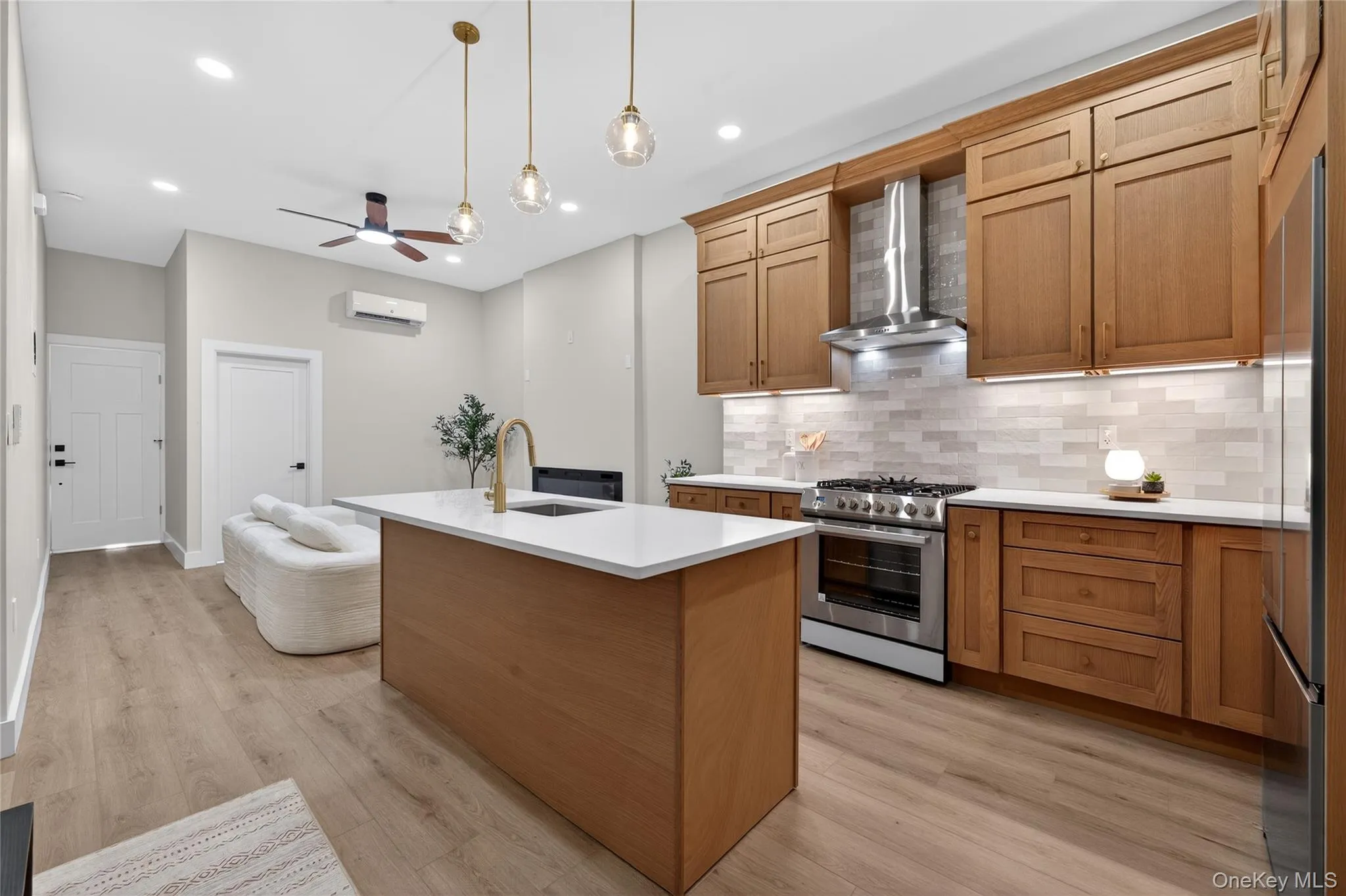Kitchen featuring a center island with sink, stainless steel appliances, wood-finish cabinetry, light-toned backsplash, and recessed lighting Kitchen featuring a center island with sink, stainless steel appliances, wood-finish cabinetry, light-toned backsplash, and recessed lighting